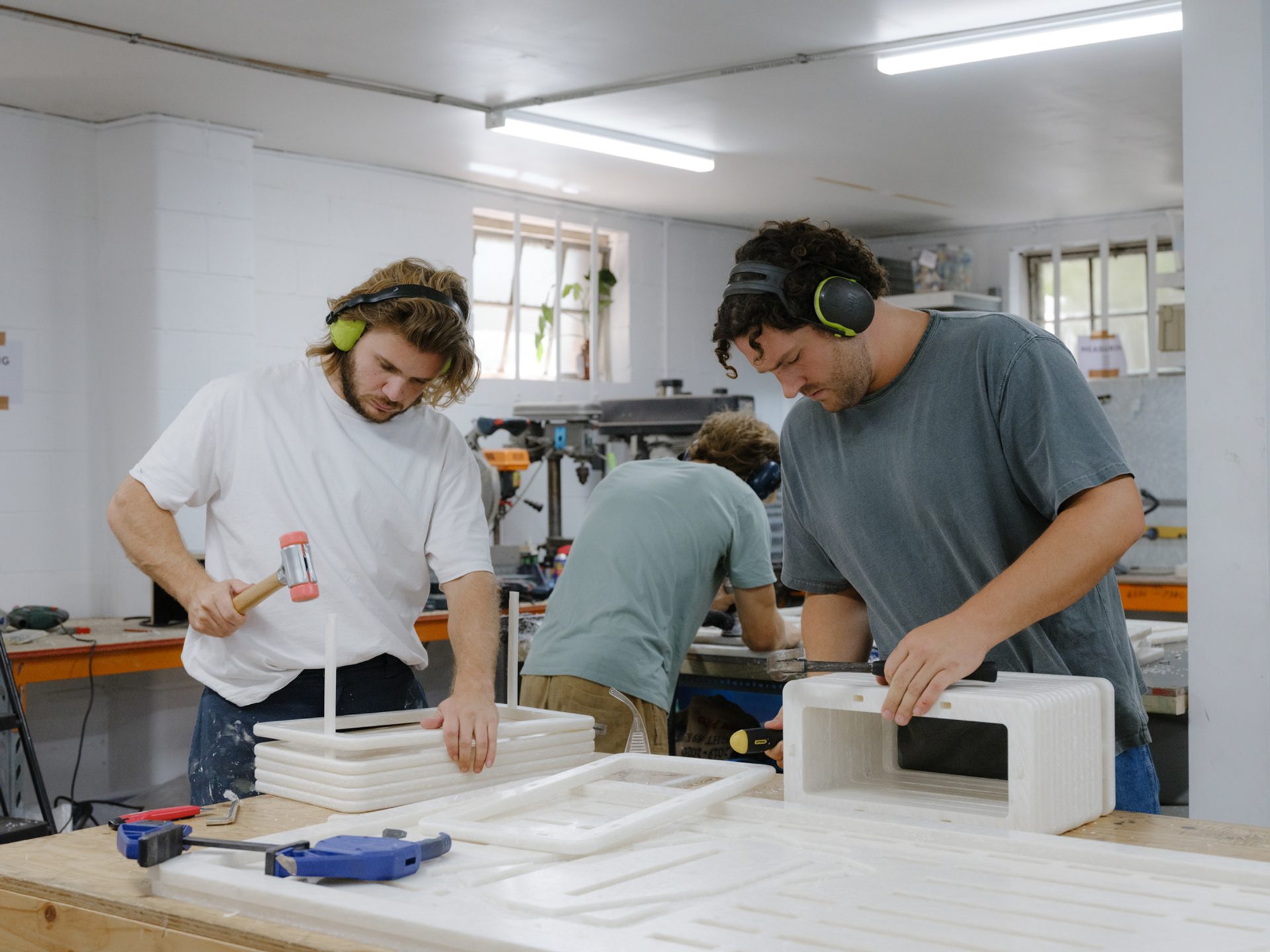 Figures wearing ear safety gear, and hammering together pieces of a product.