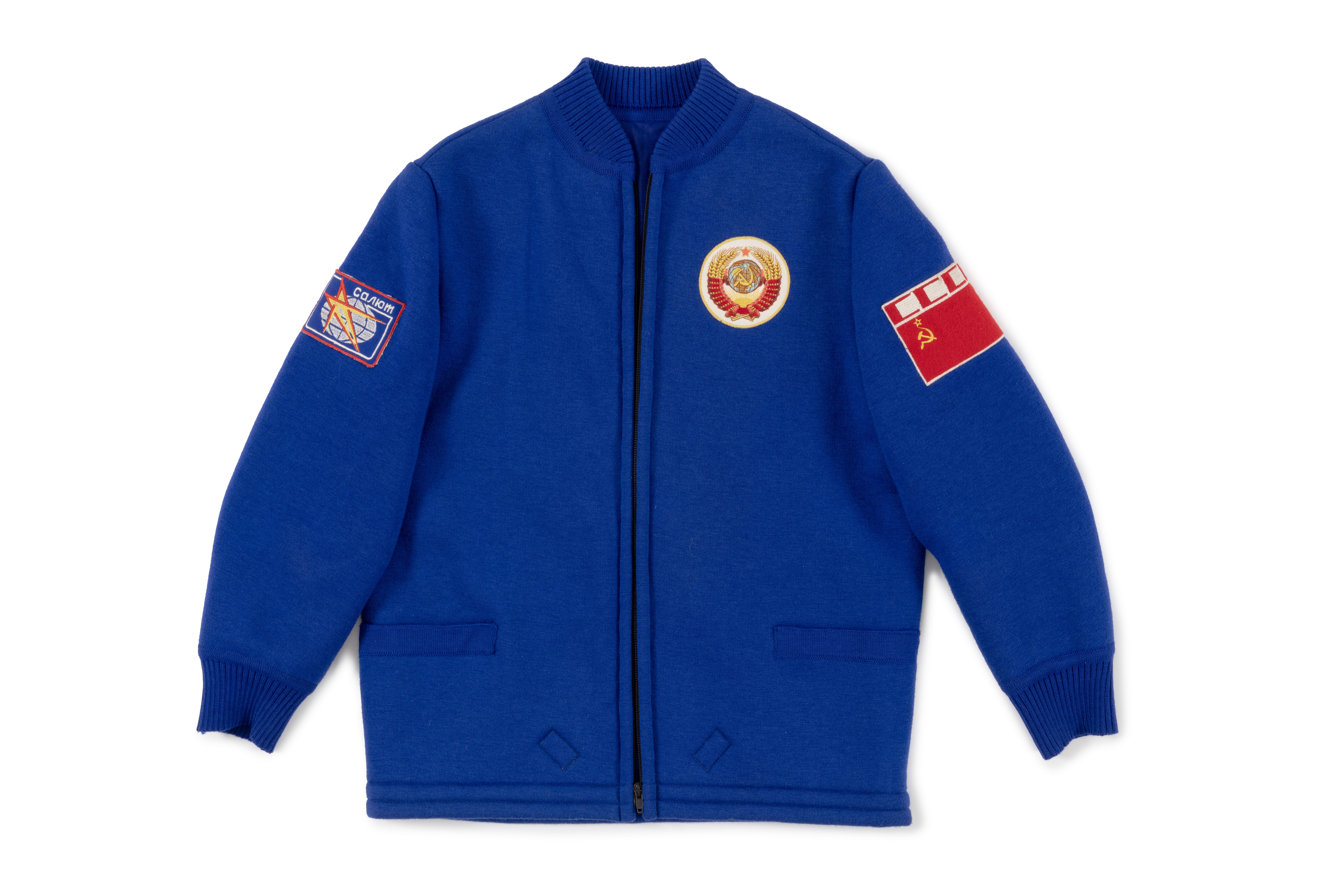 Photograph of the heavy jacket a part of a five piece royal blue polyester wool blend flight suit with white trims, emblems and patches.