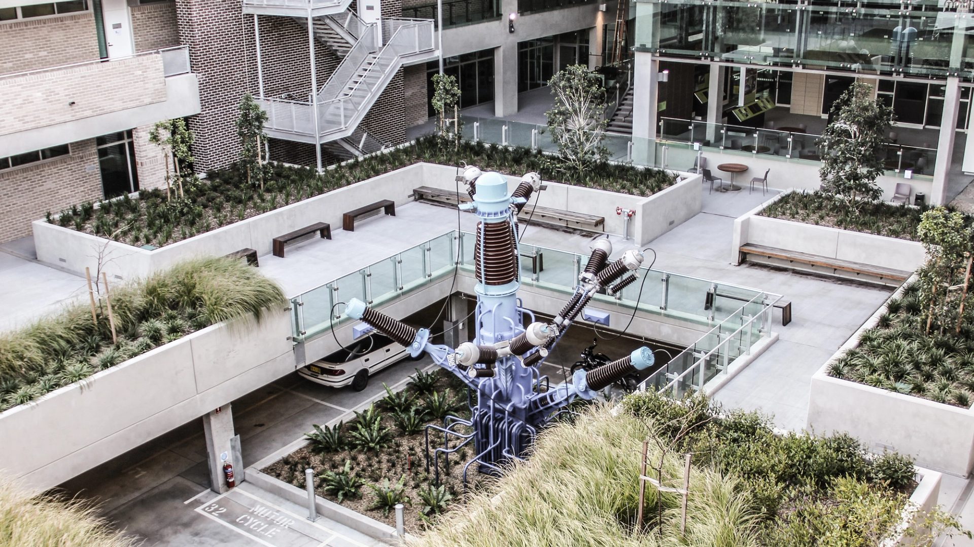 The courtyard of a building containing grasses, glass panels and a central sculpture.