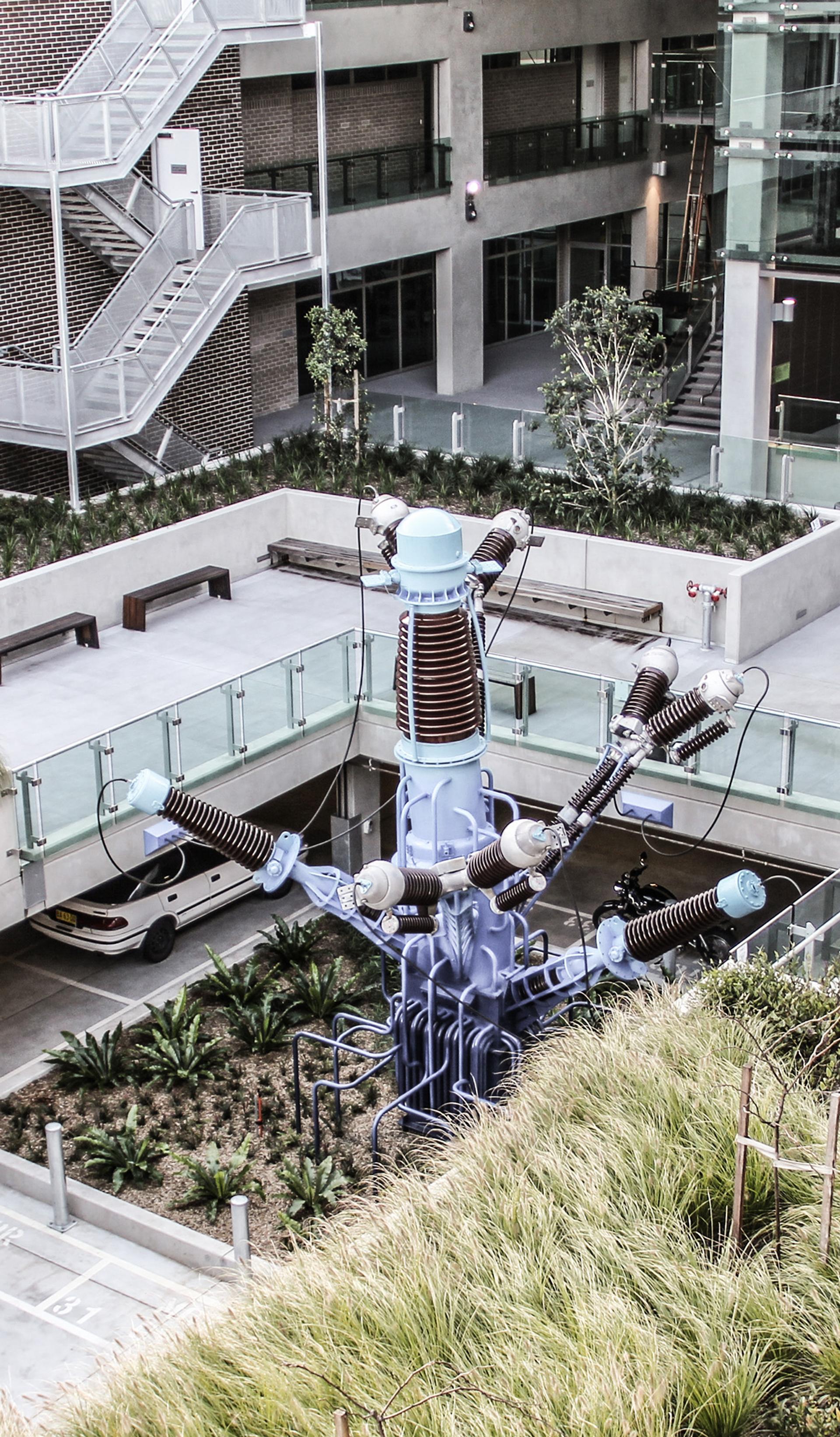 The courtyard of a building containing grasses, glass panels and a central sculpture.