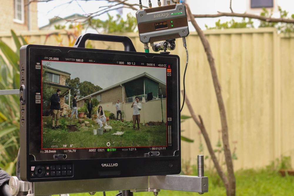 A shot of a small HD screen, reflecting filming. On the screen a group of 6 people are in a suburuban backyard.