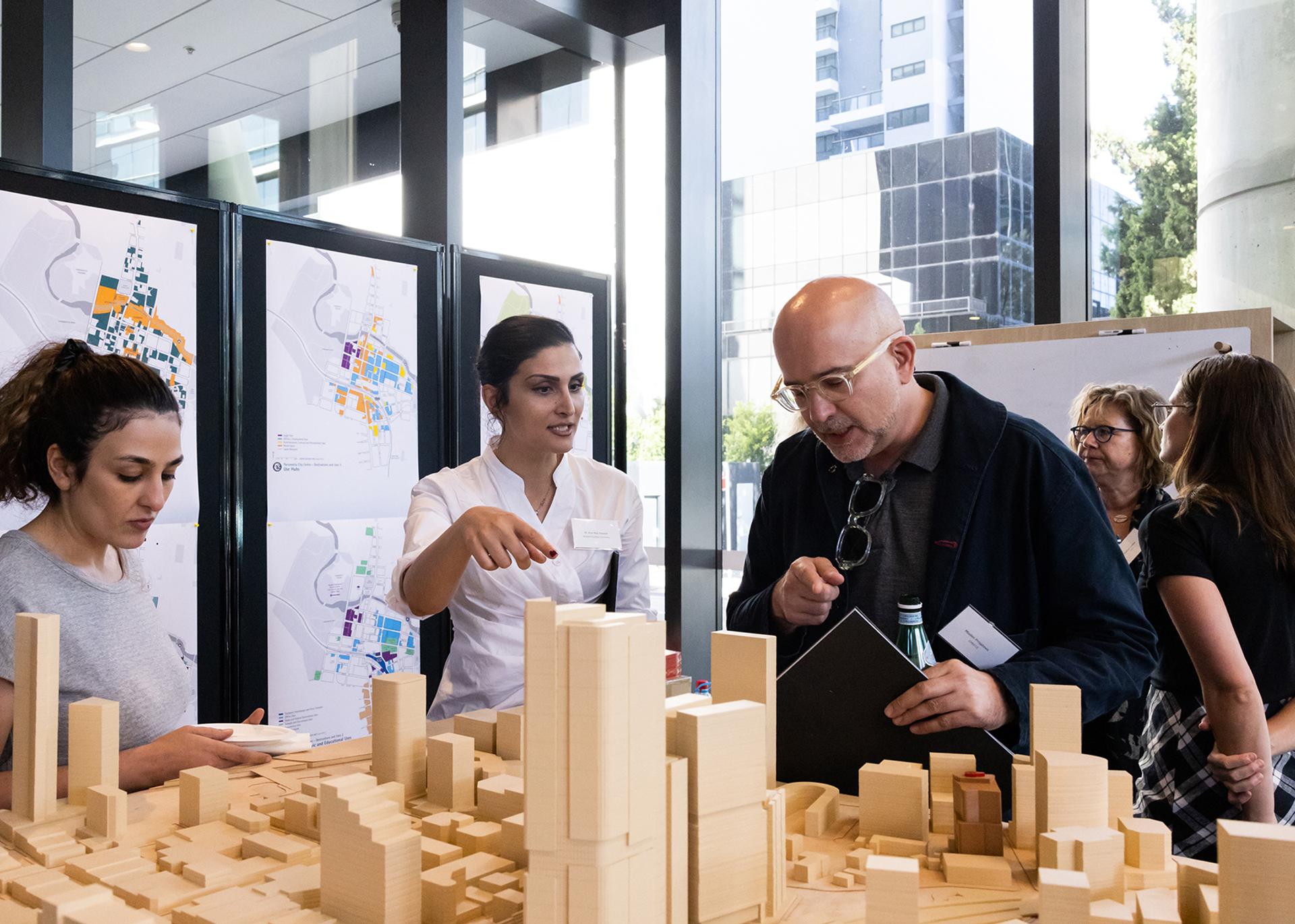People talking and looking over a wooden model of a city.
