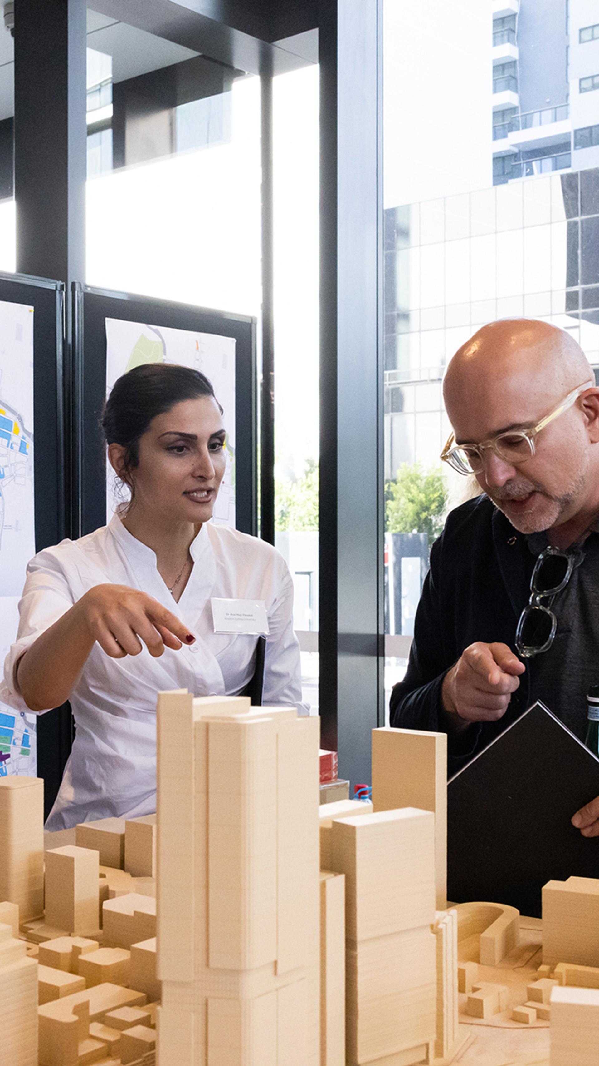 People talking and looking over a wooden model of a city.