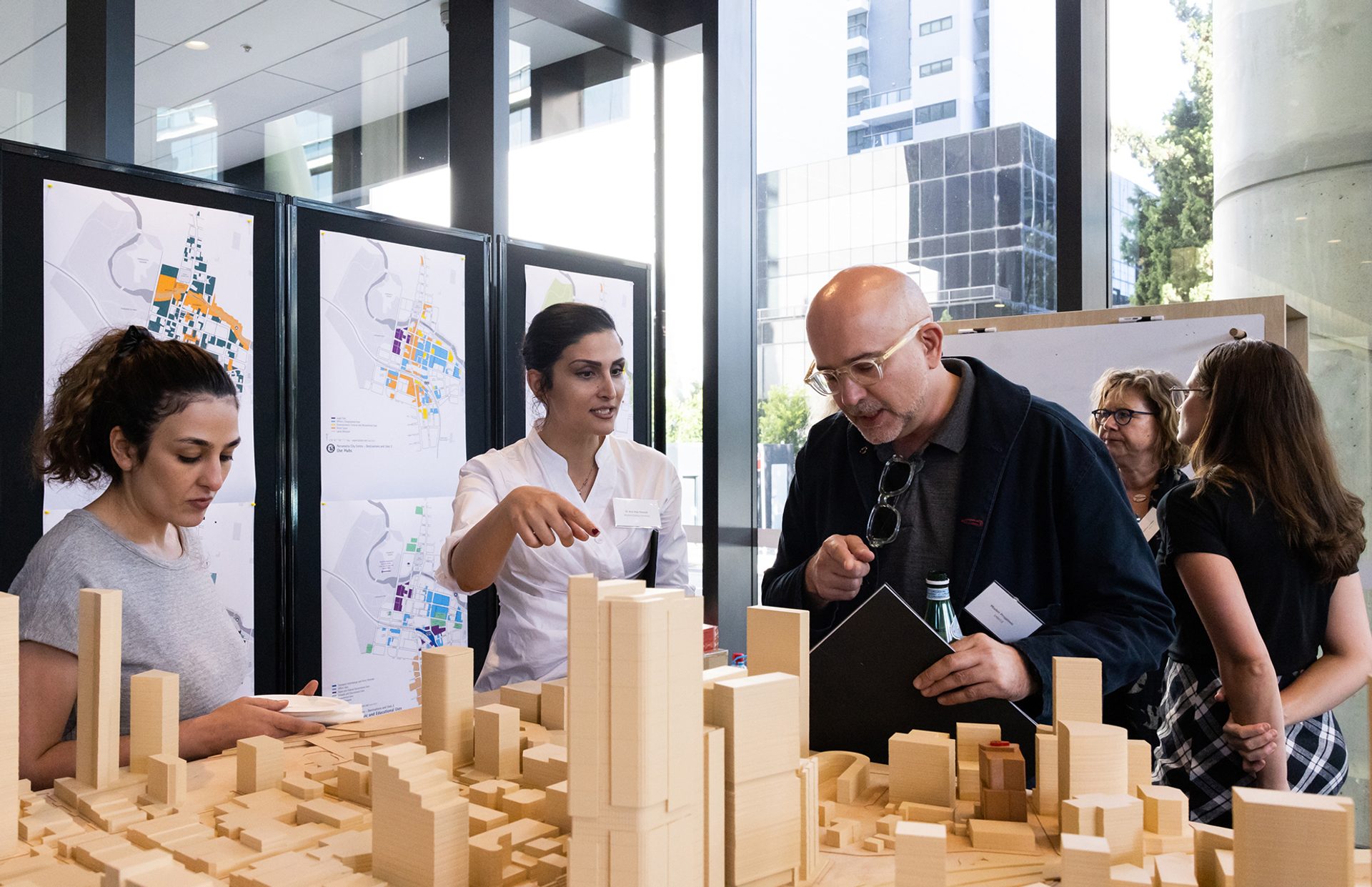 People talking and looking over a wooden model of a city.