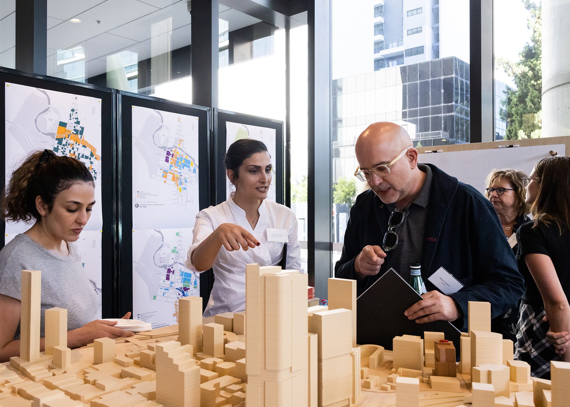 People talking and looking over a wooden model of a city.