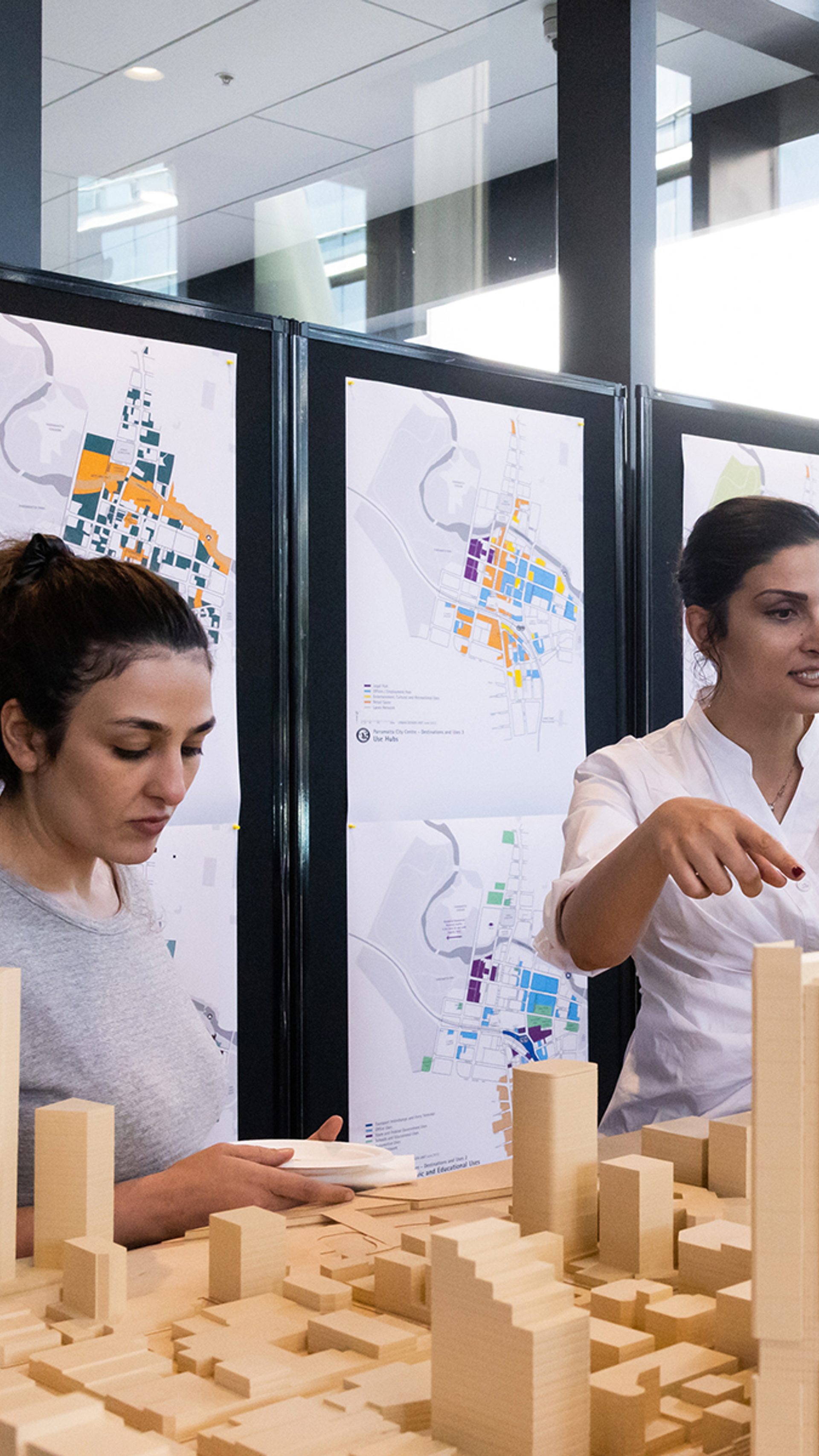 People talking and looking over a wooden model of a city.