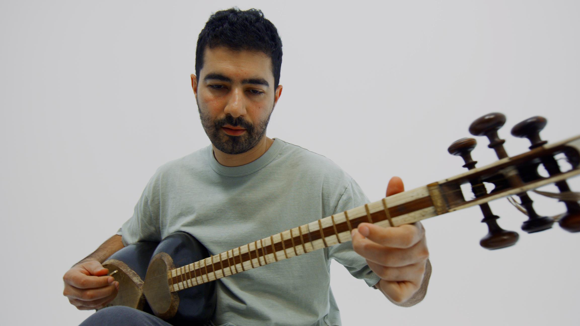 Hamed Sadeghi sits in a white room performing on the Persian tar musical instrument.