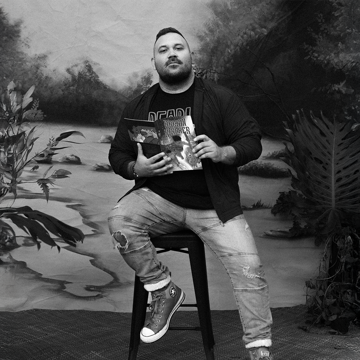 A Gooniyandi Gajerrong man sits on a stool and holds an Indigenous comic.