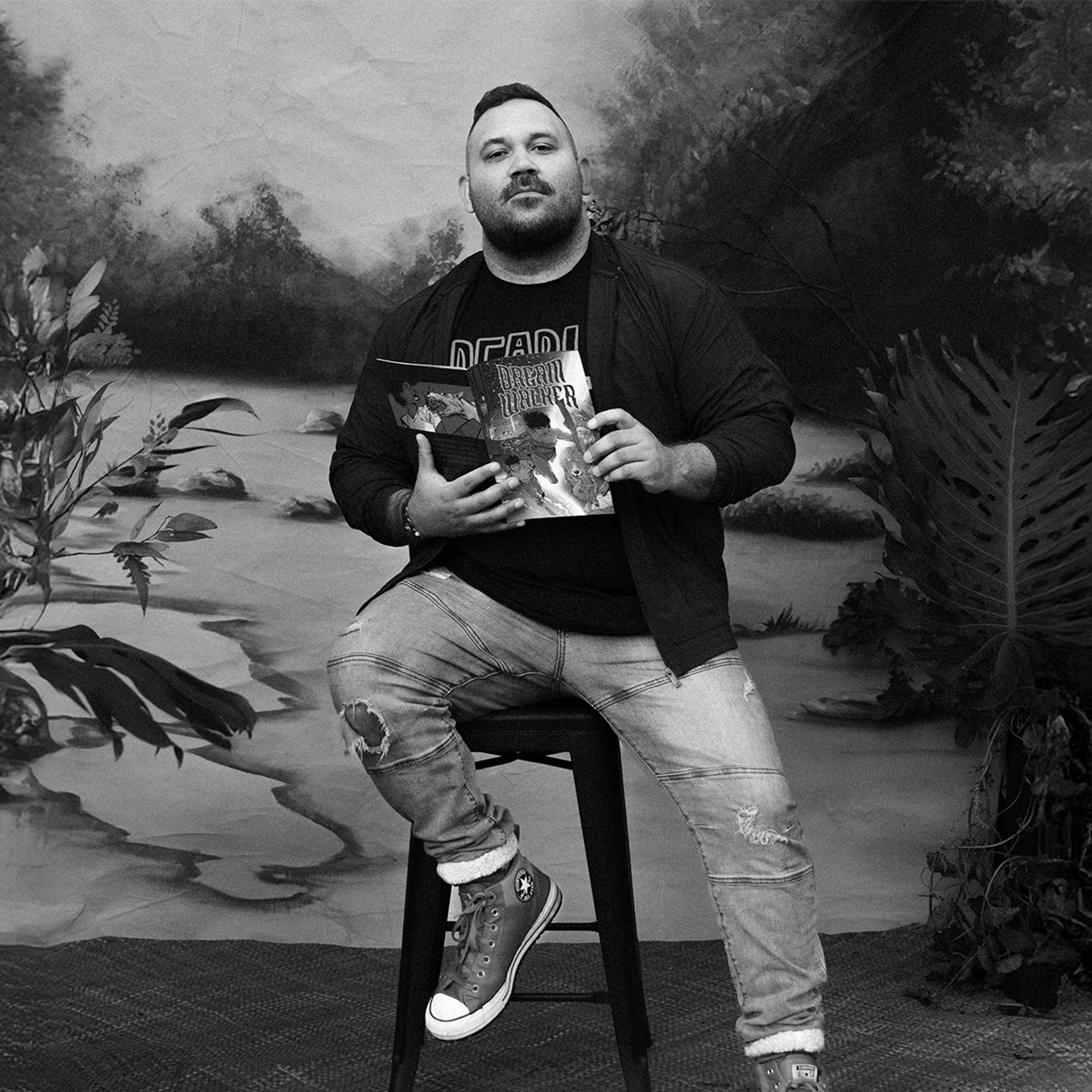 A Gooniyandi Gajerrong man sits on a stool and holds an Indigenous comic.