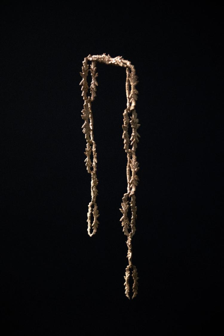 A gold necklace imitating the shapes of coral on a black background