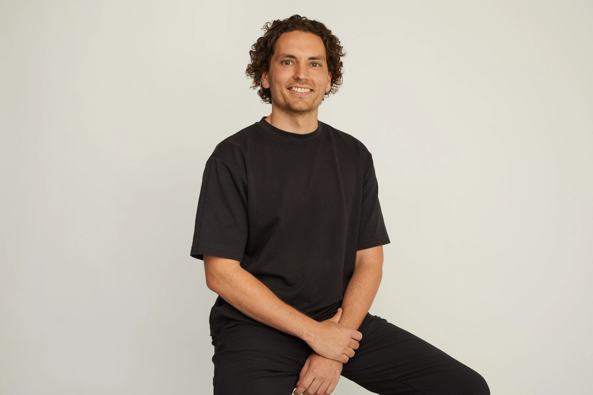 Man wearing all black sits looking at camera.