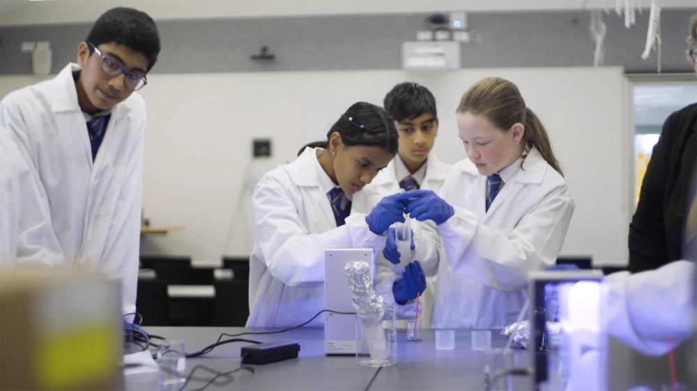 Four students in lab coats and blue gloves work together on an experiment.