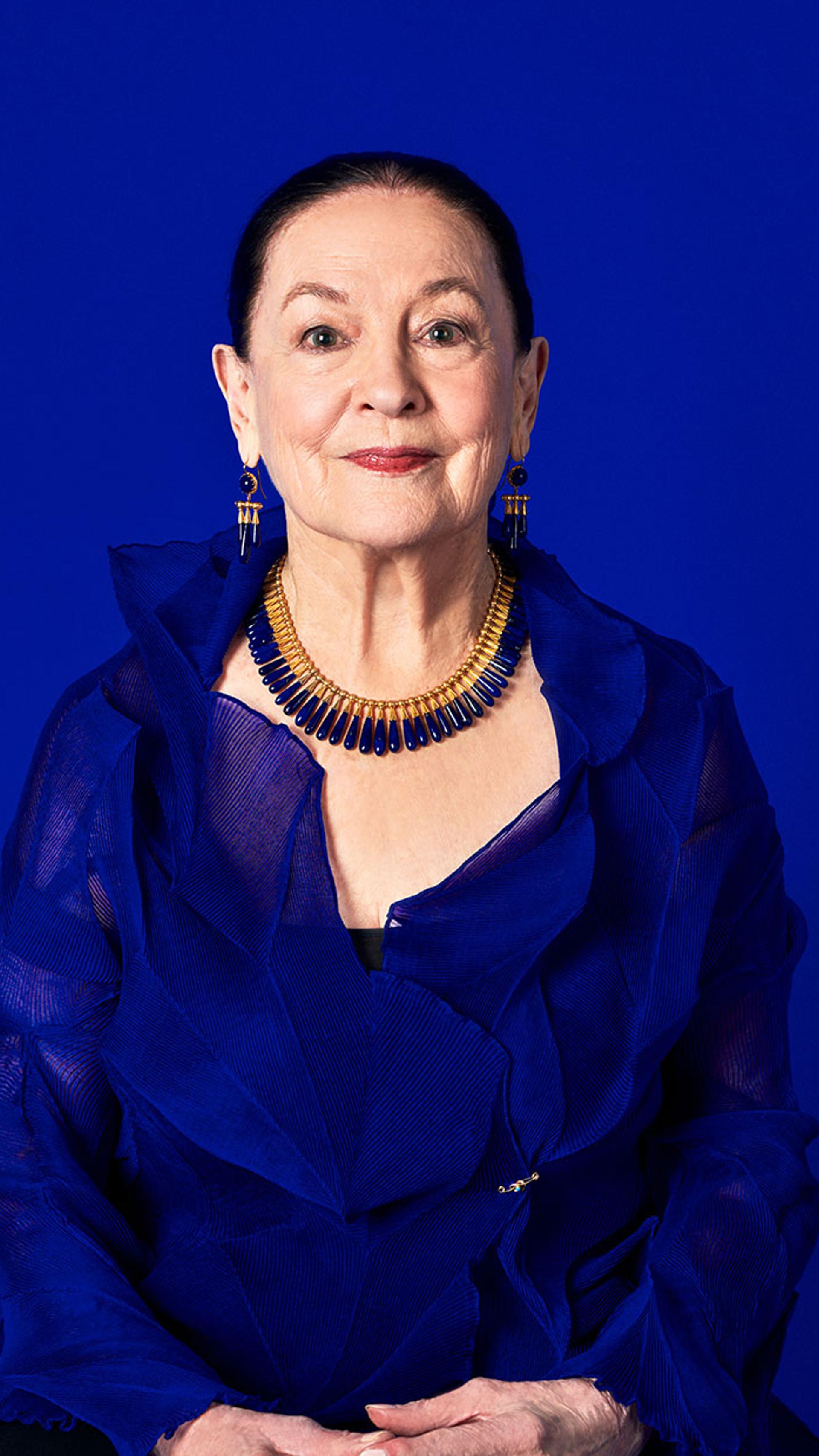Portrait of a woman with dark hair slicked back wearing a blue and gold necklace with matching earrings.