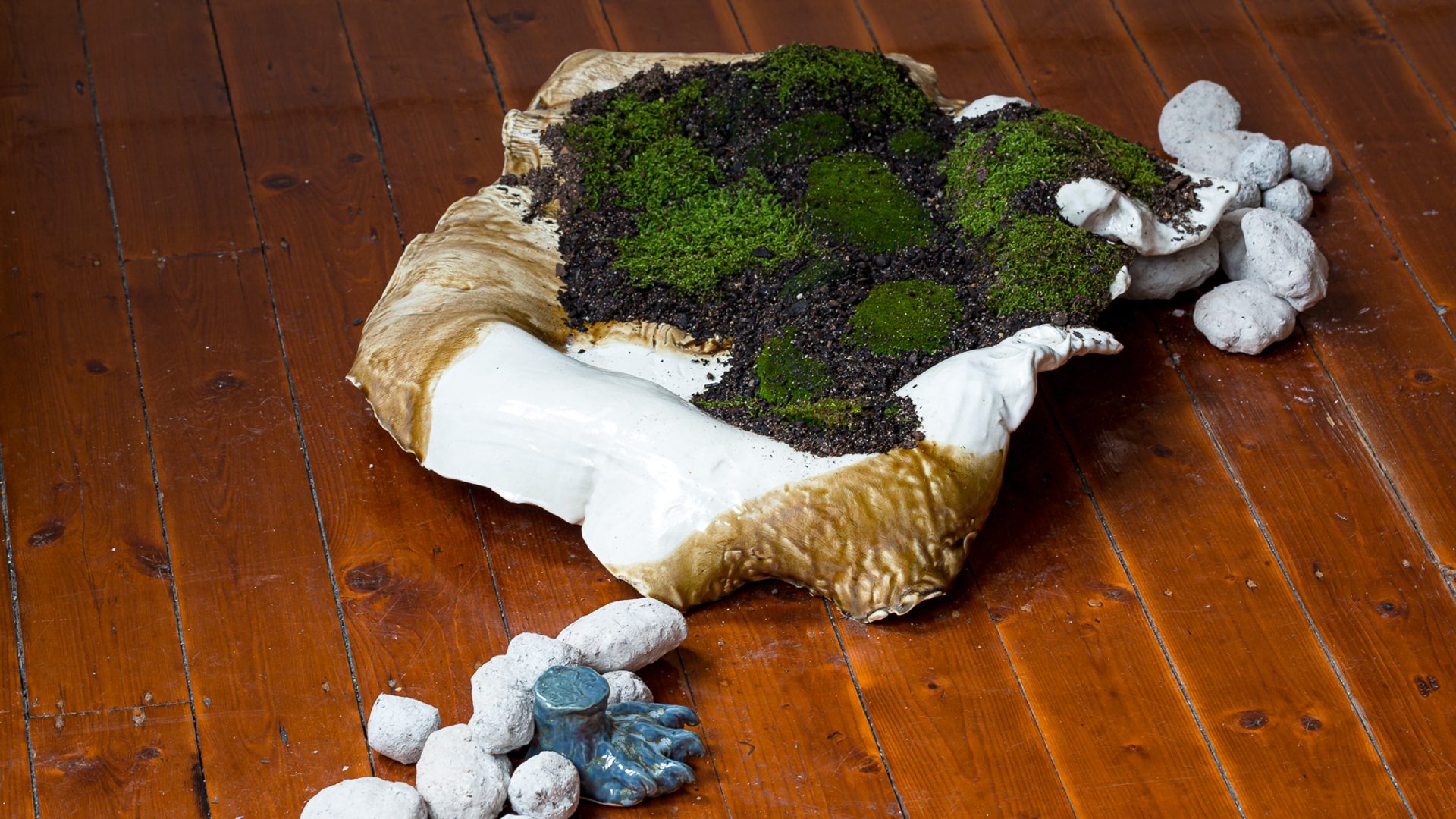 A shell like mound, of glazed raku sits on the floorboards filled with dirt and moss