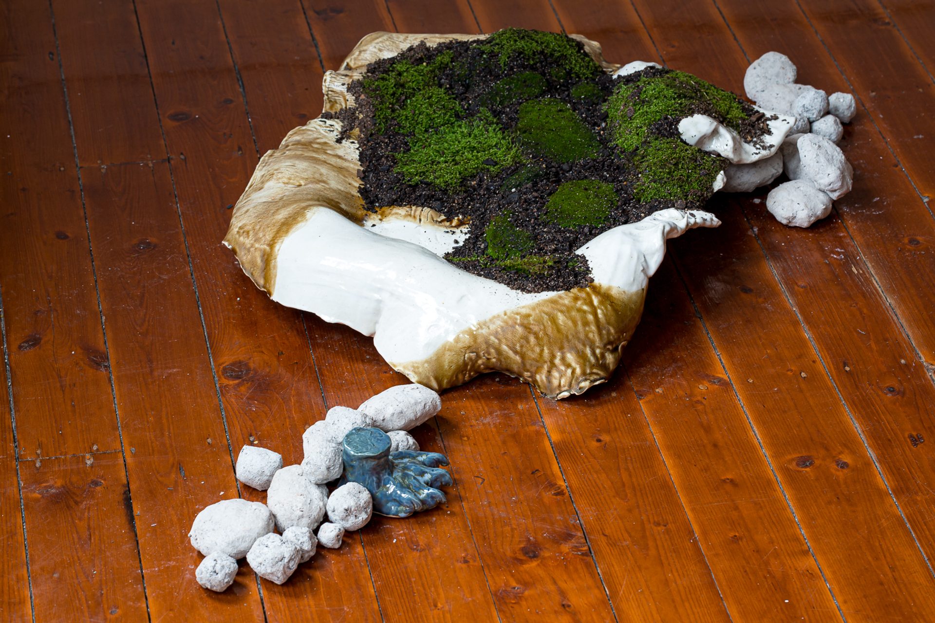 A shell like mound, of glazed raku sits on the floorboards filled with dirt and moss