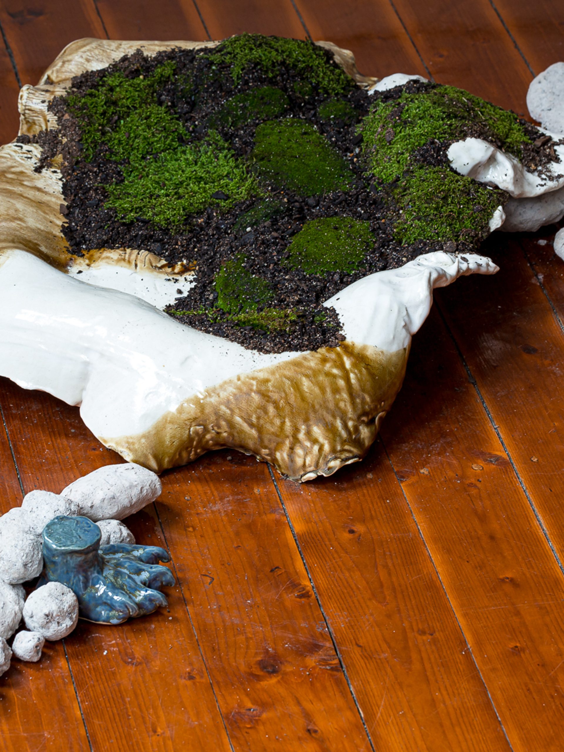 A shell like mound, of glazed raku sits on the floorboards filled with dirt and moss