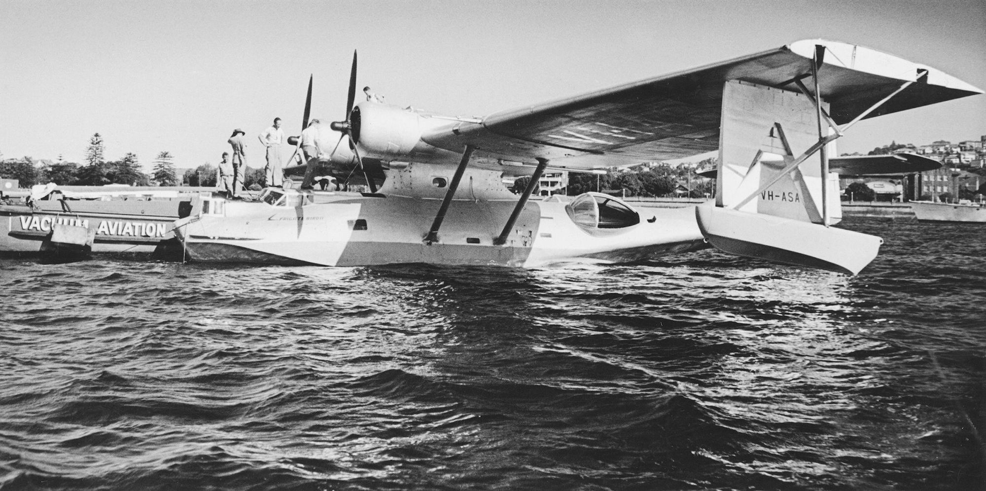 The Catalina is on the water. Four men stand atop it. Black and white photograph.