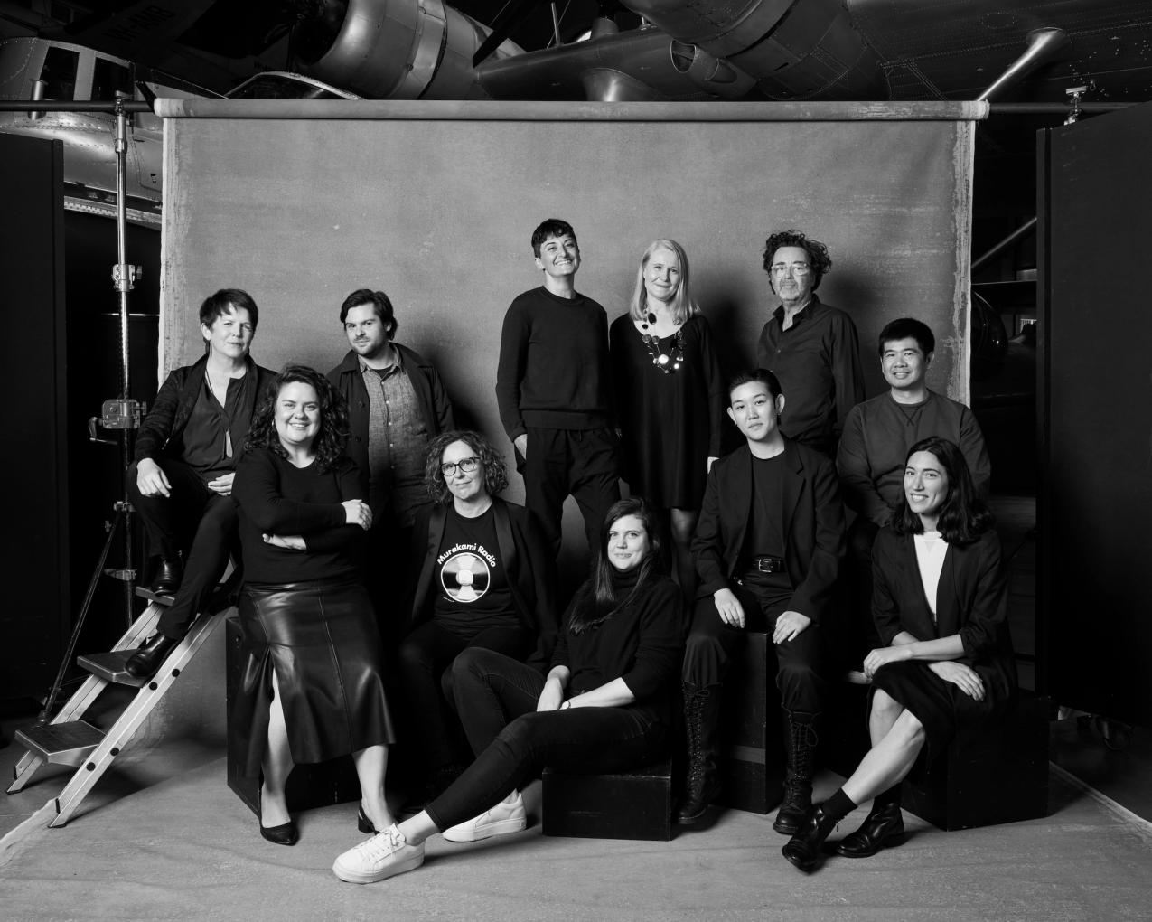 Group of people in black clothing pose in front of a background in a photo studio