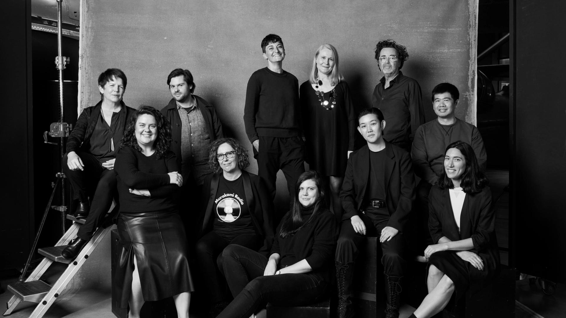 Group of people in black clothing pose in front of a background in a photo studio