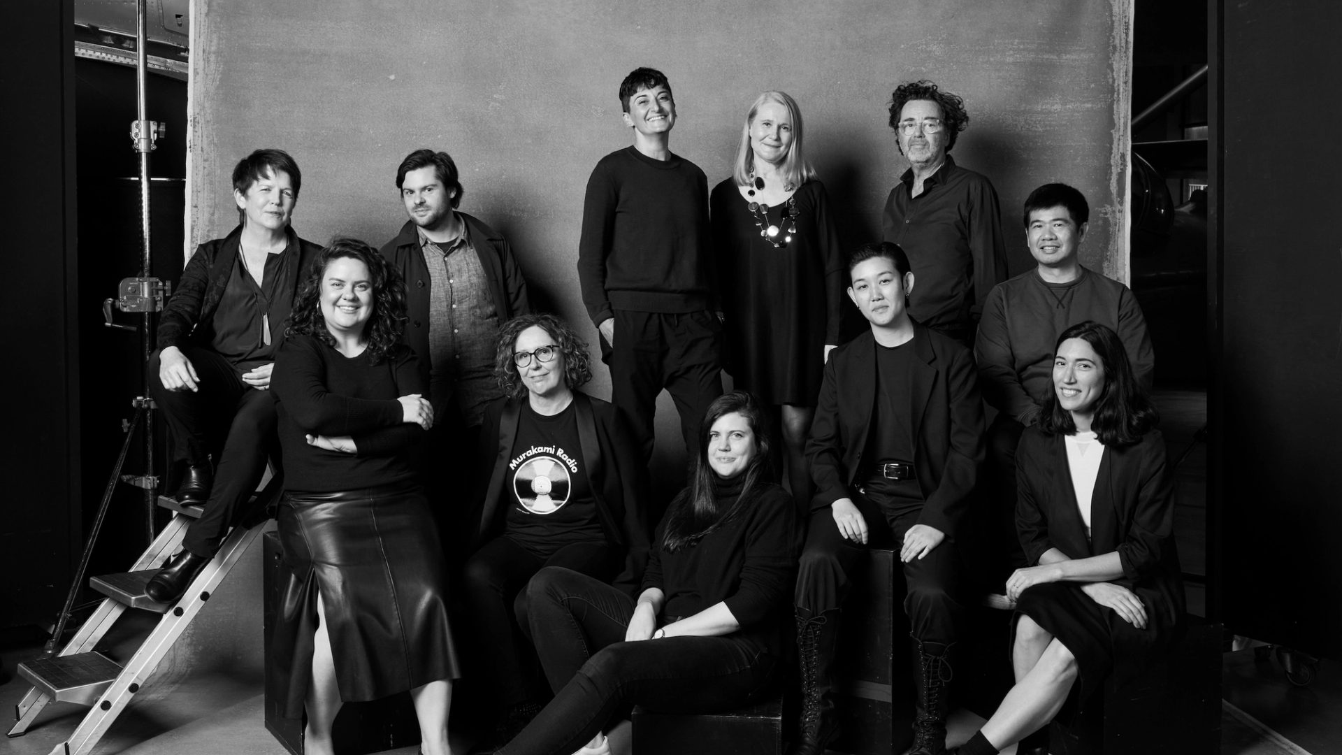 Group of people in black clothing pose in front of a background in a photo studio
