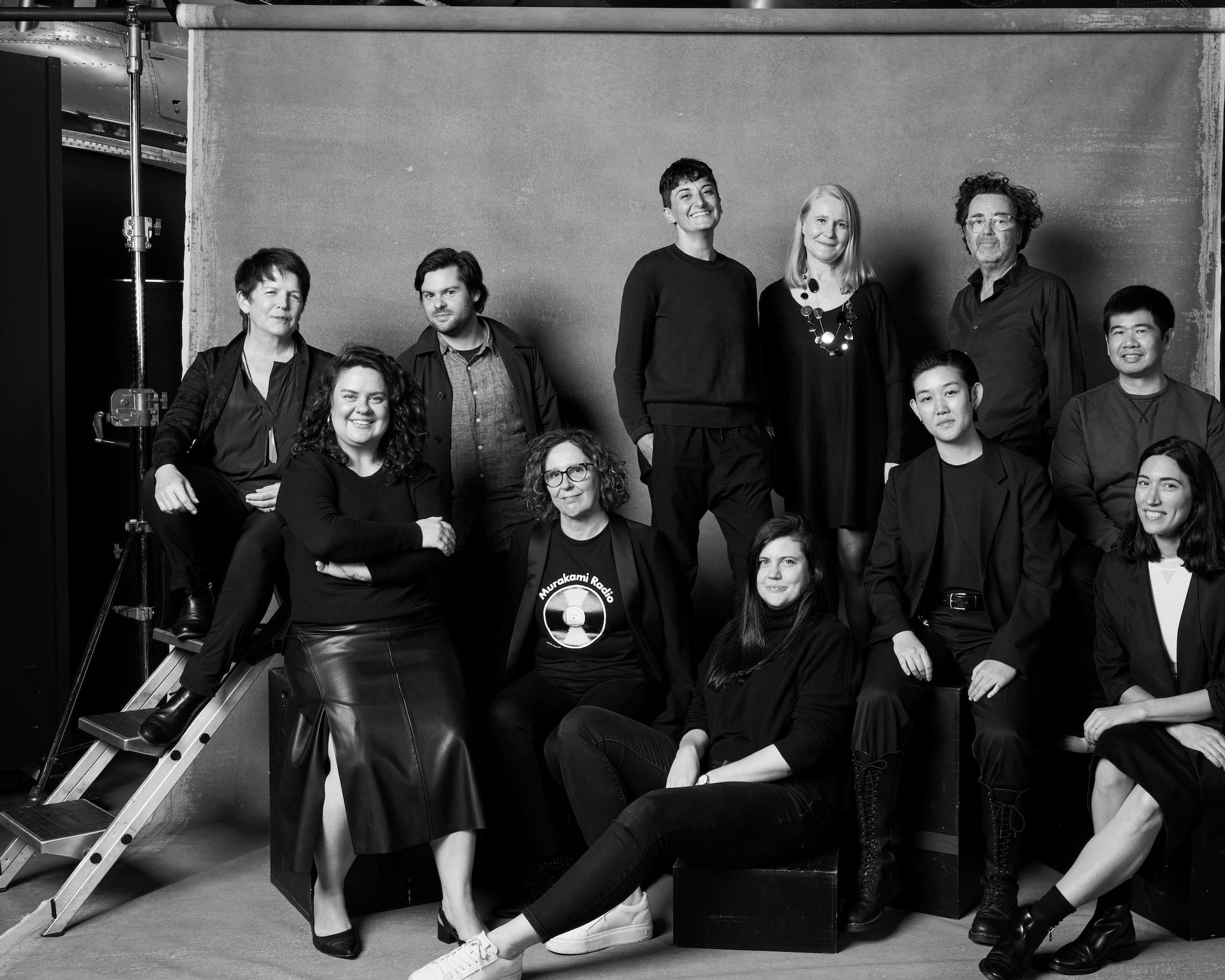 Group of people in black clothing pose in front of a background in a photo studio