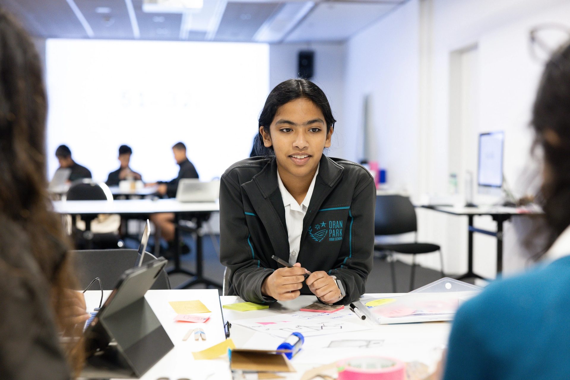 School kid leans over desk with pens in hand