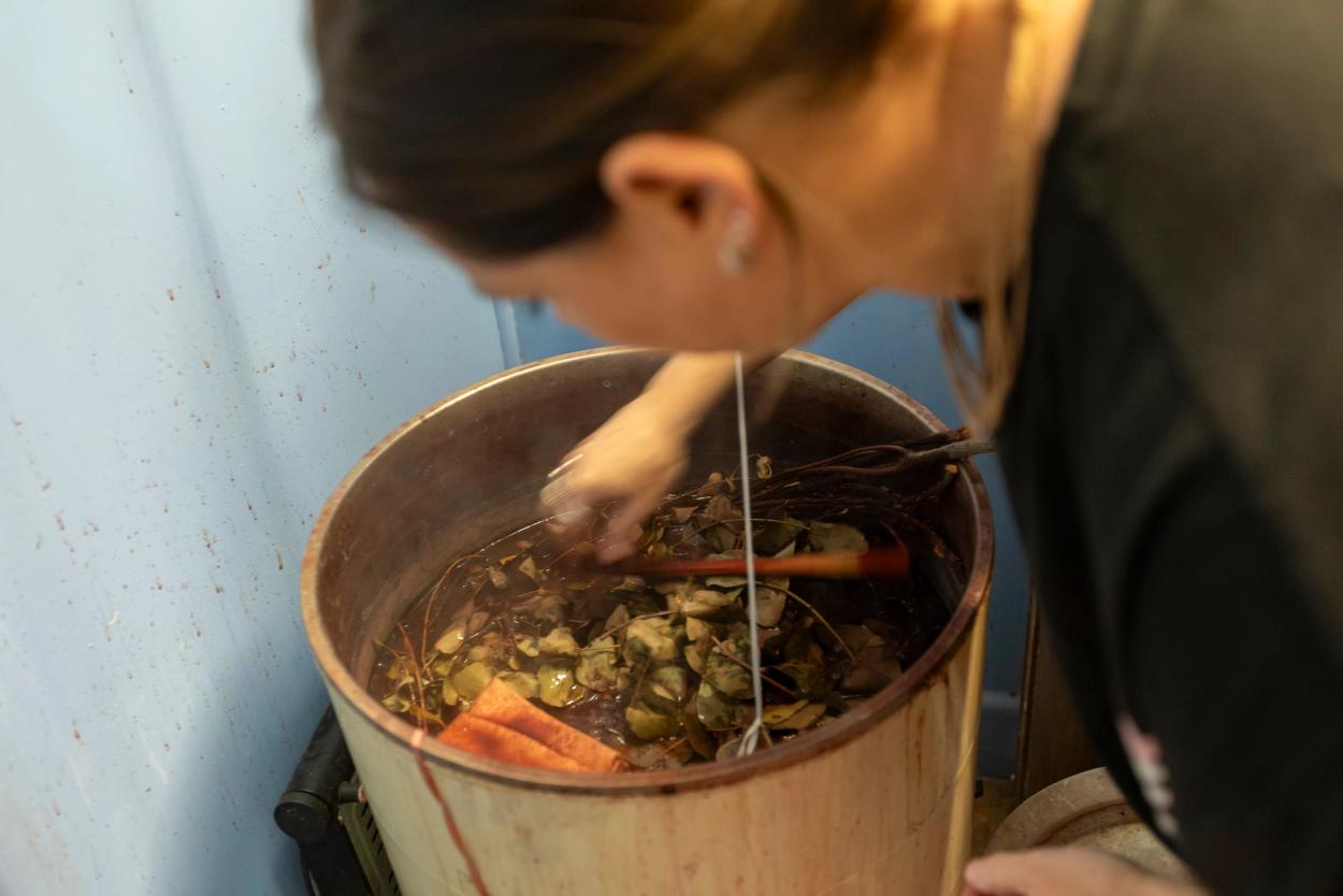 A woman leaning over and mixing a large vat filled with various plants.