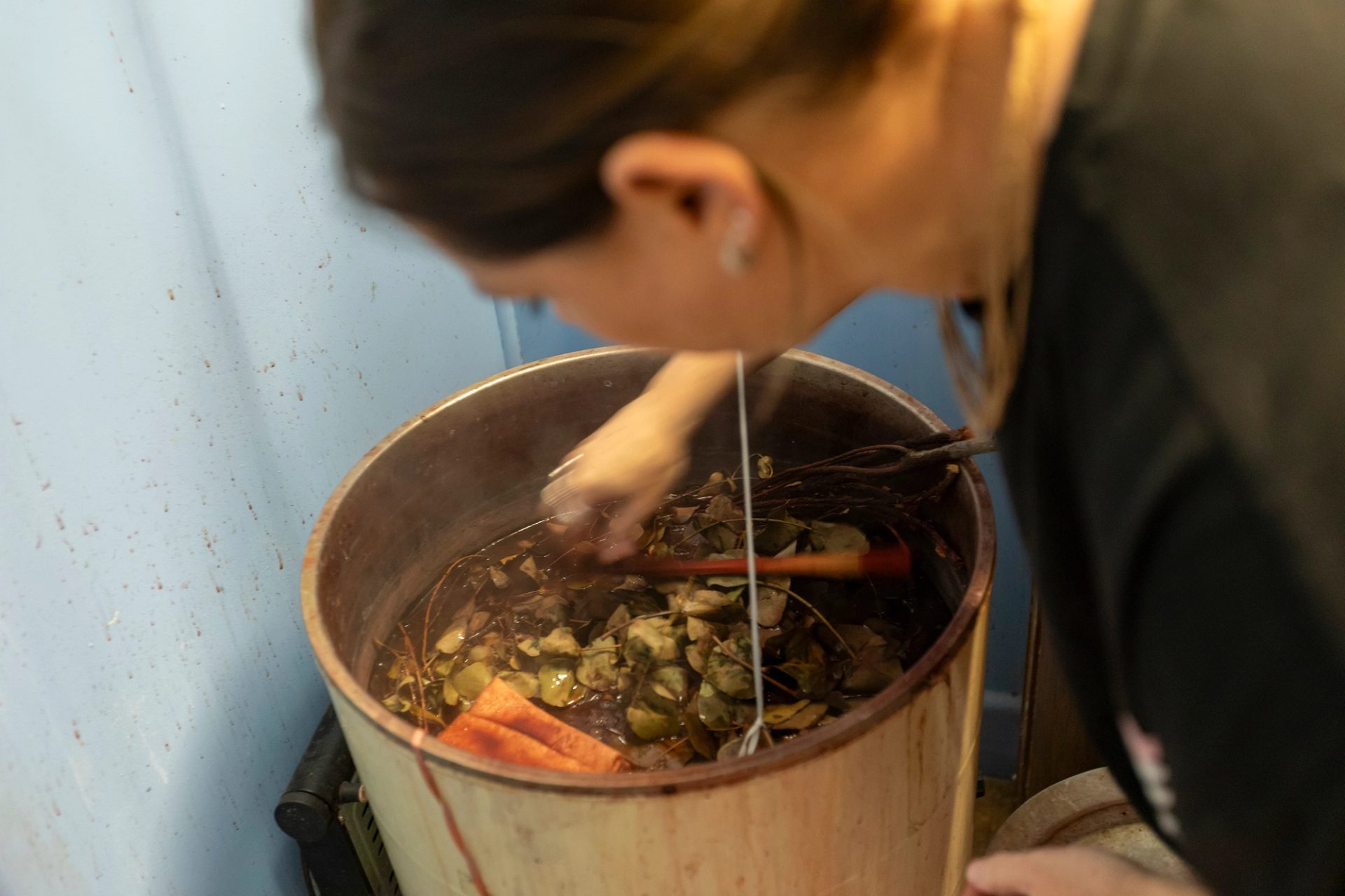 A woman leaning over and mixing a large vat filled with various plants.