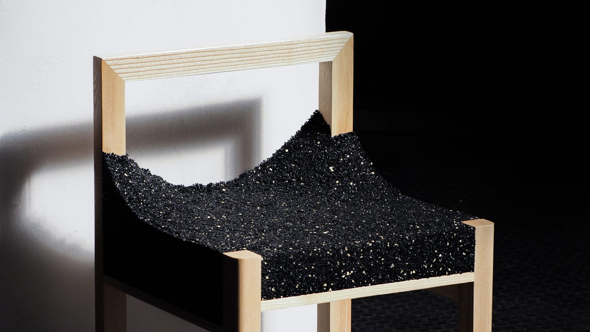 A timber framed chair with a shiny, black, uneven material.