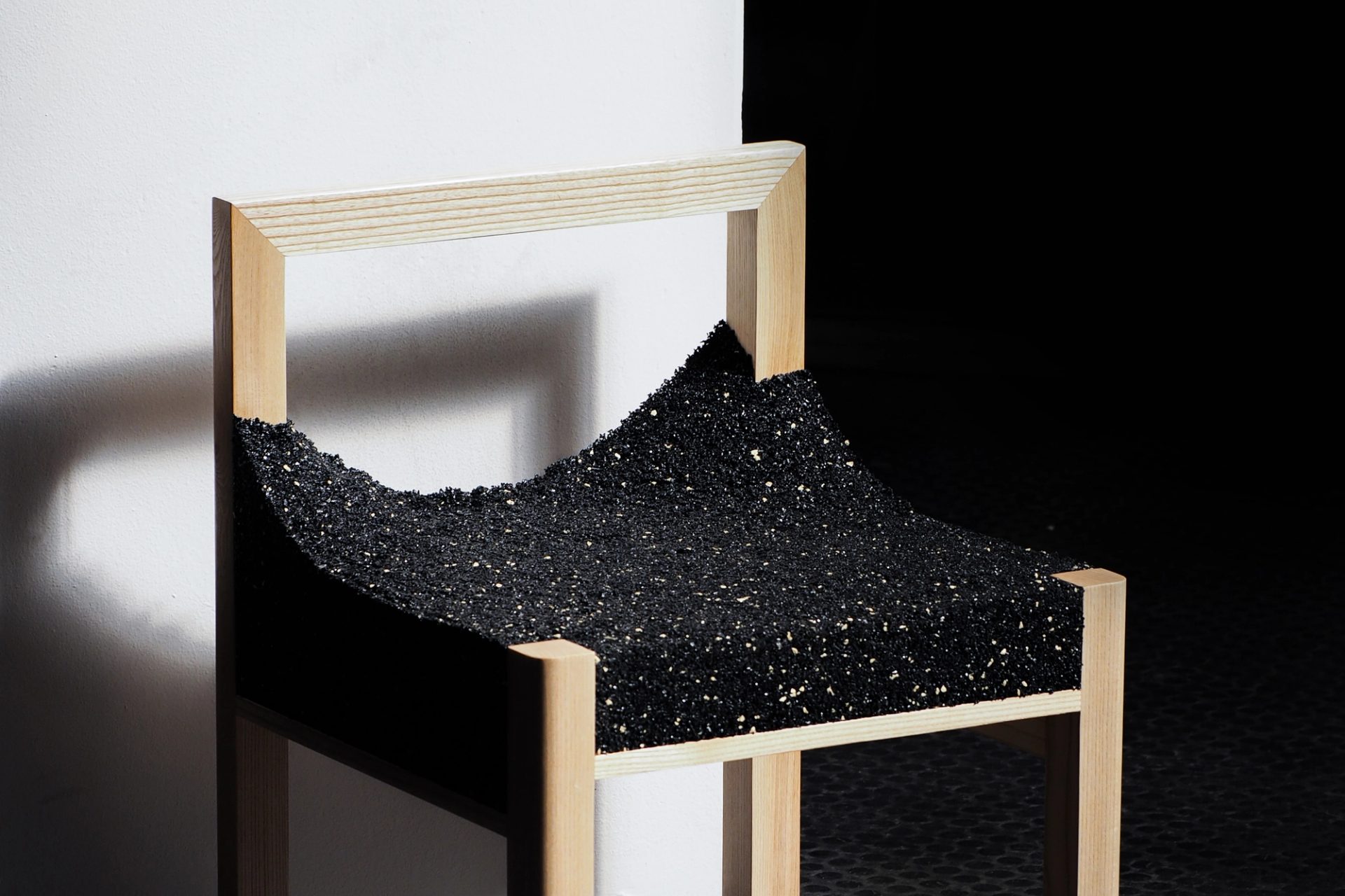 A timber framed chair with a shiny, black, uneven material.