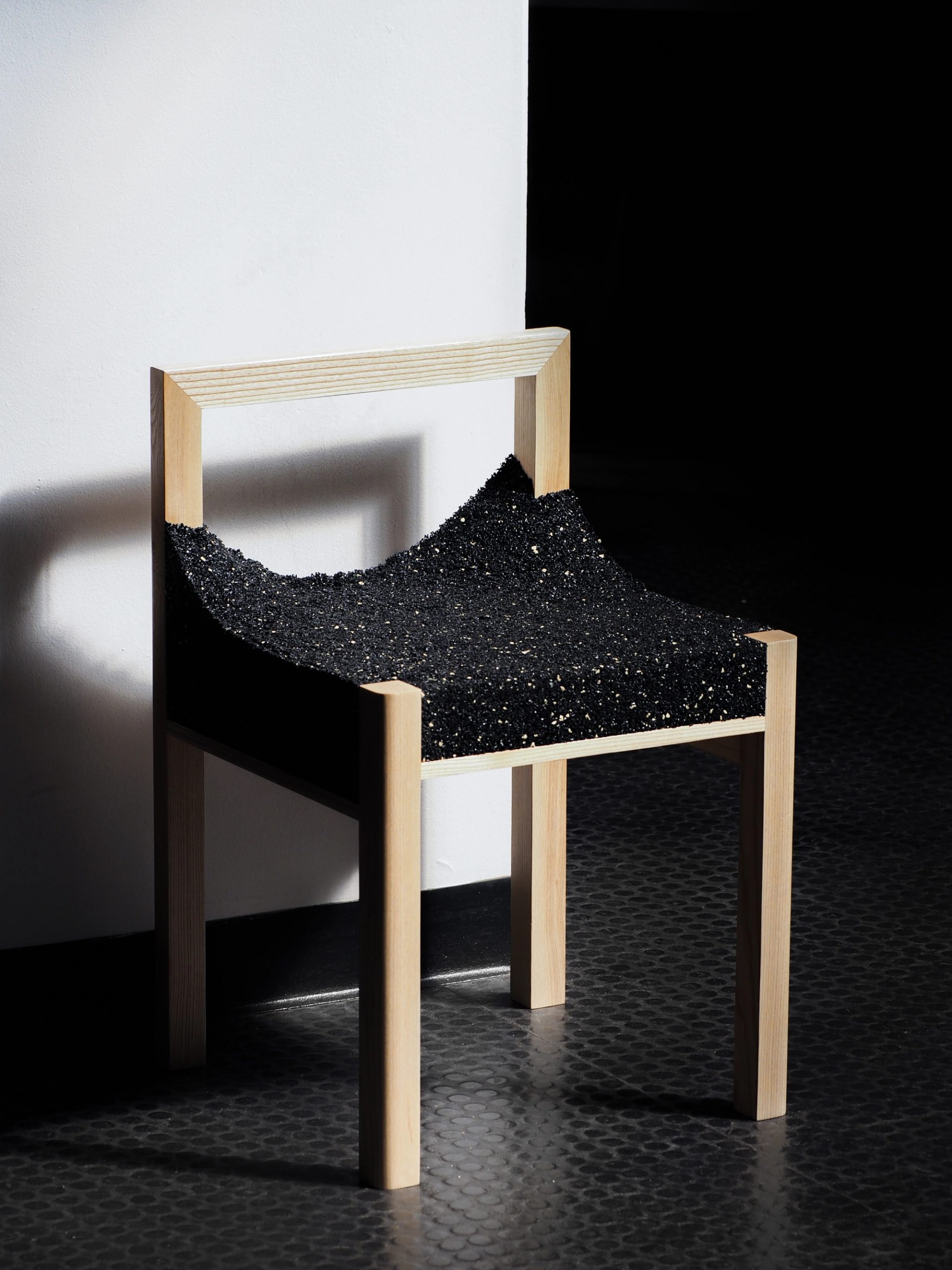 A timber framed chair with a shiny, black, uneven material.