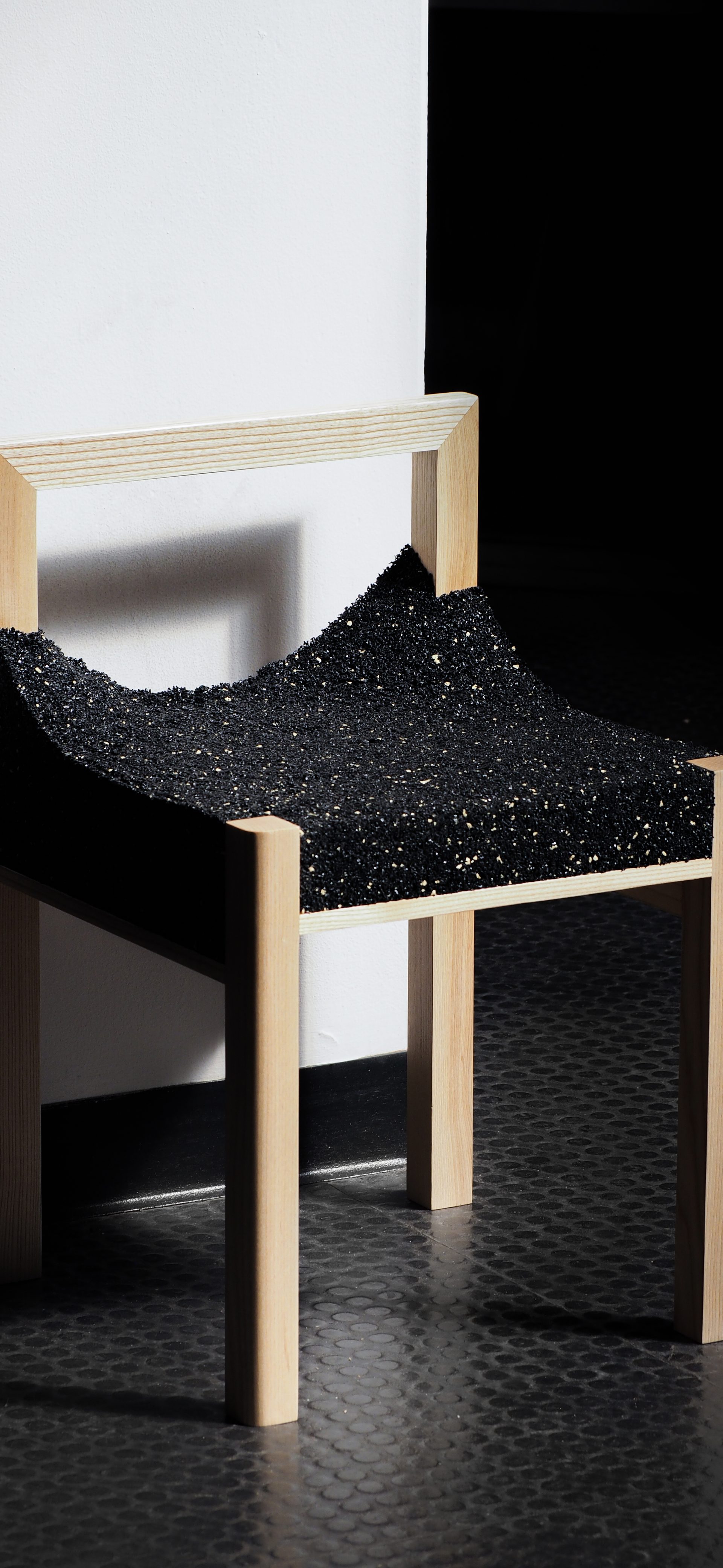A timber framed chair with a shiny, black, uneven material.