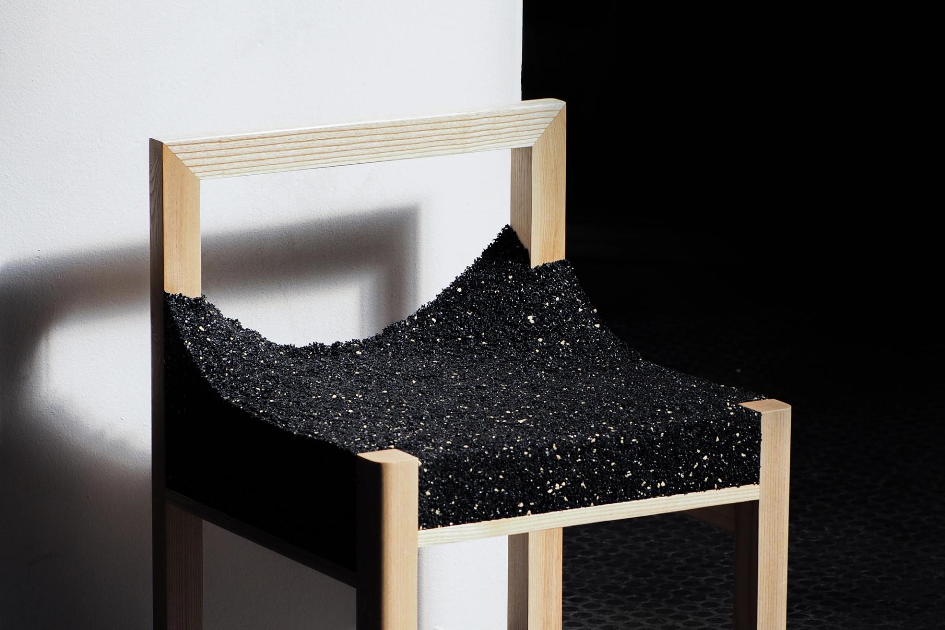 A timber framed chair with a shiny, black, uneven material.
