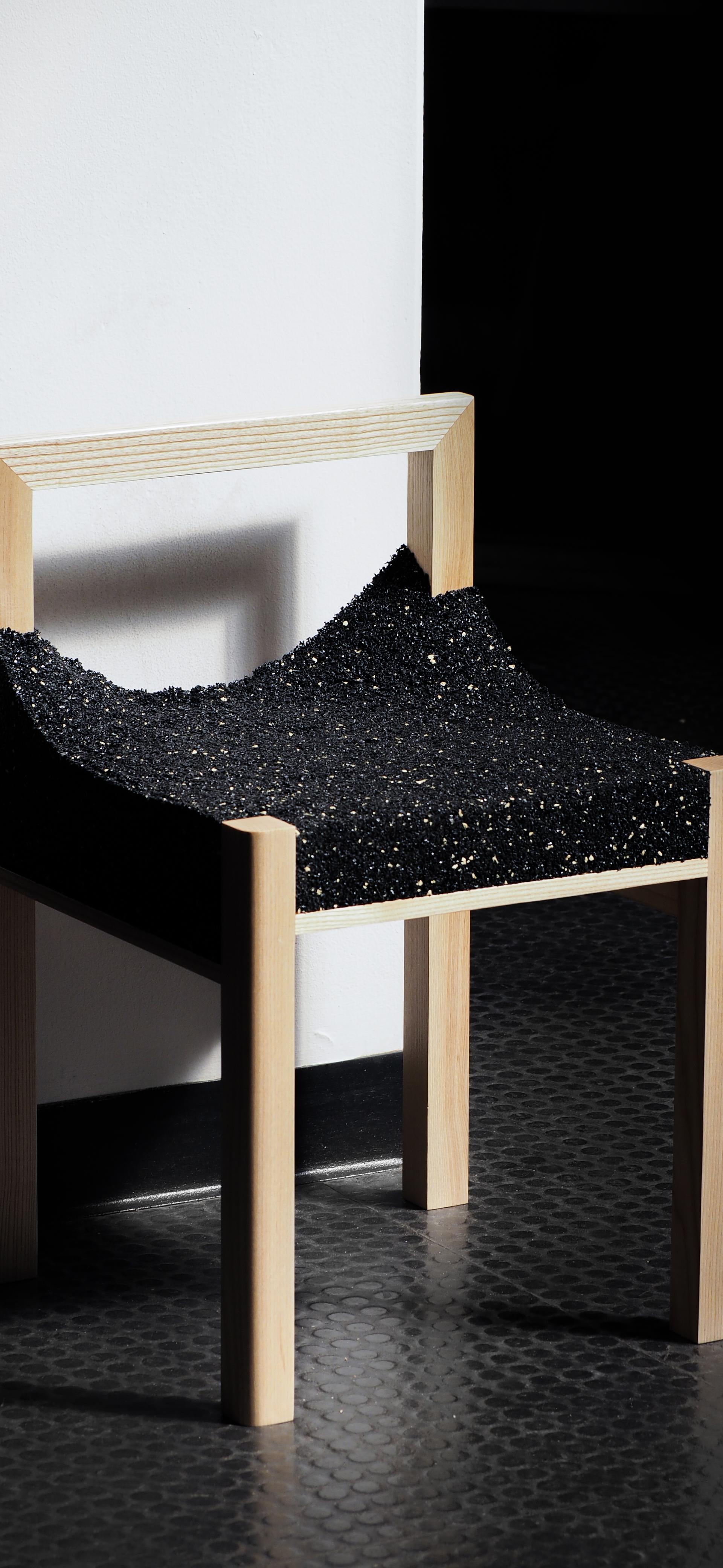 A timber framed chair with a shiny, black, uneven material.