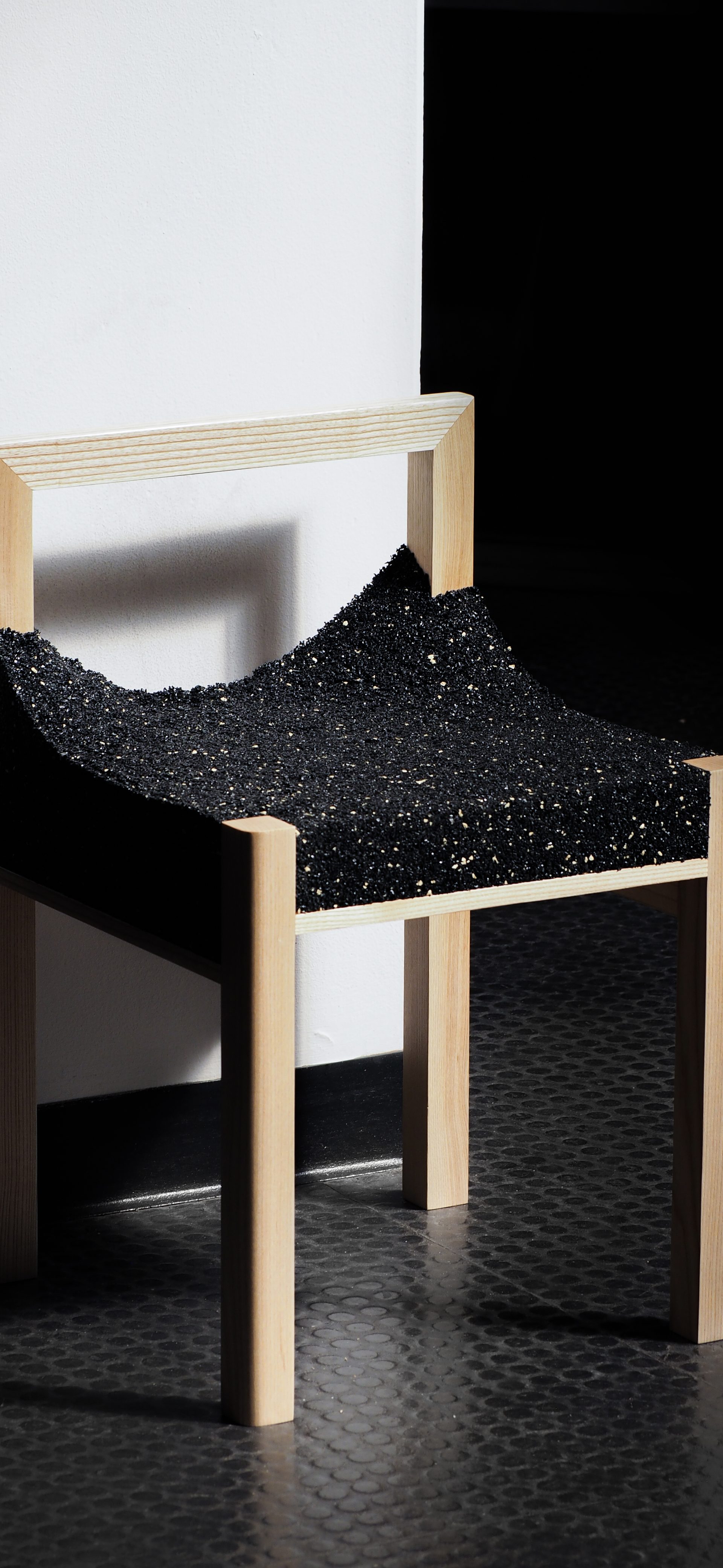 A timber framed chair with a shiny, black, uneven material.