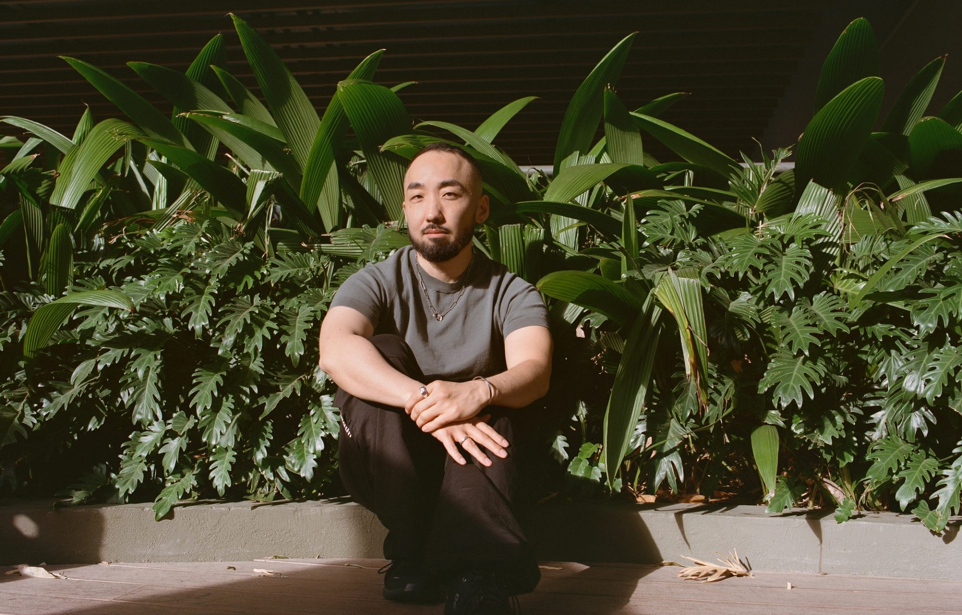 Figure sits on curb of garden bed, in front of greenery.