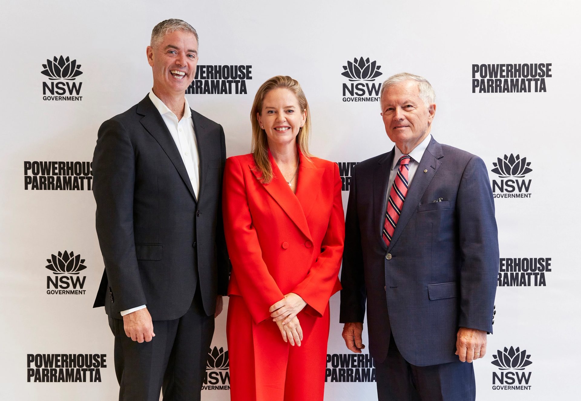 Three people in suits stand smiling at camera.