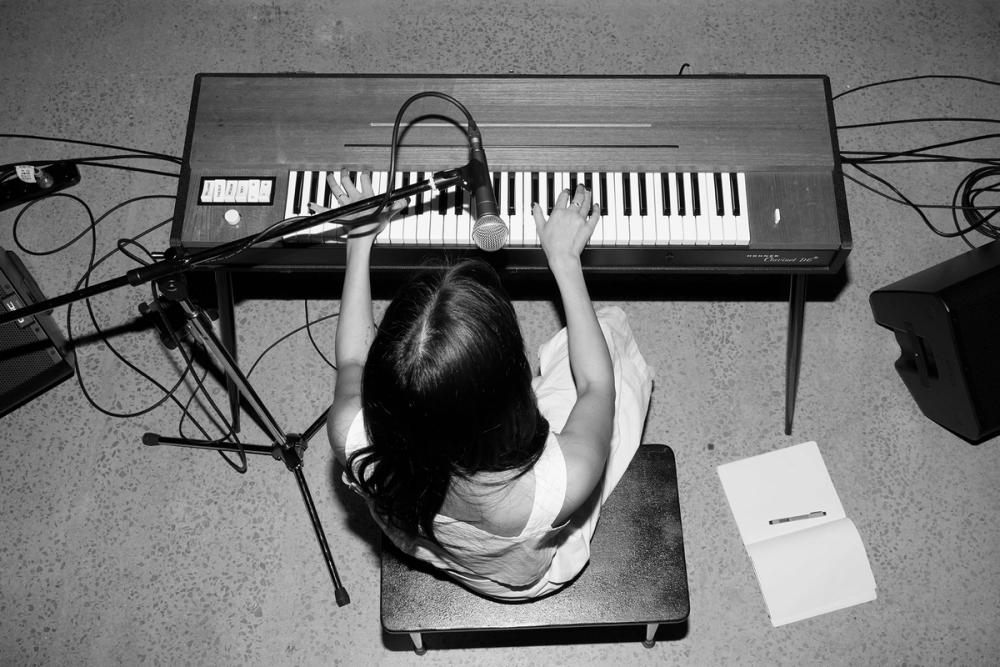 A black and white aerial shot of performer sitting at a keyboard with a microphone.
