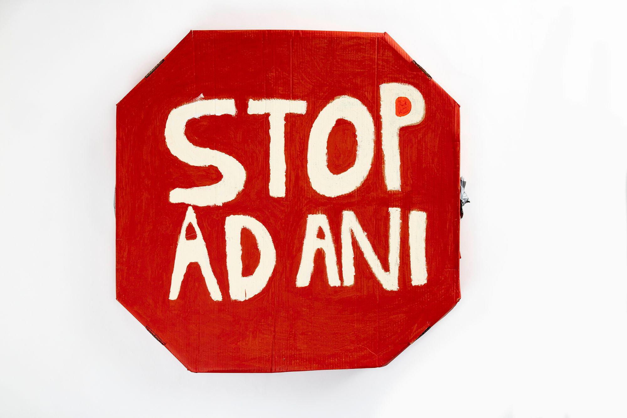 The placard is made from cardboard, and fashioned in an octagon to reflect the shape of a traffic stop sign. It is painted red, with the words 'Stop Adani' painted in white.