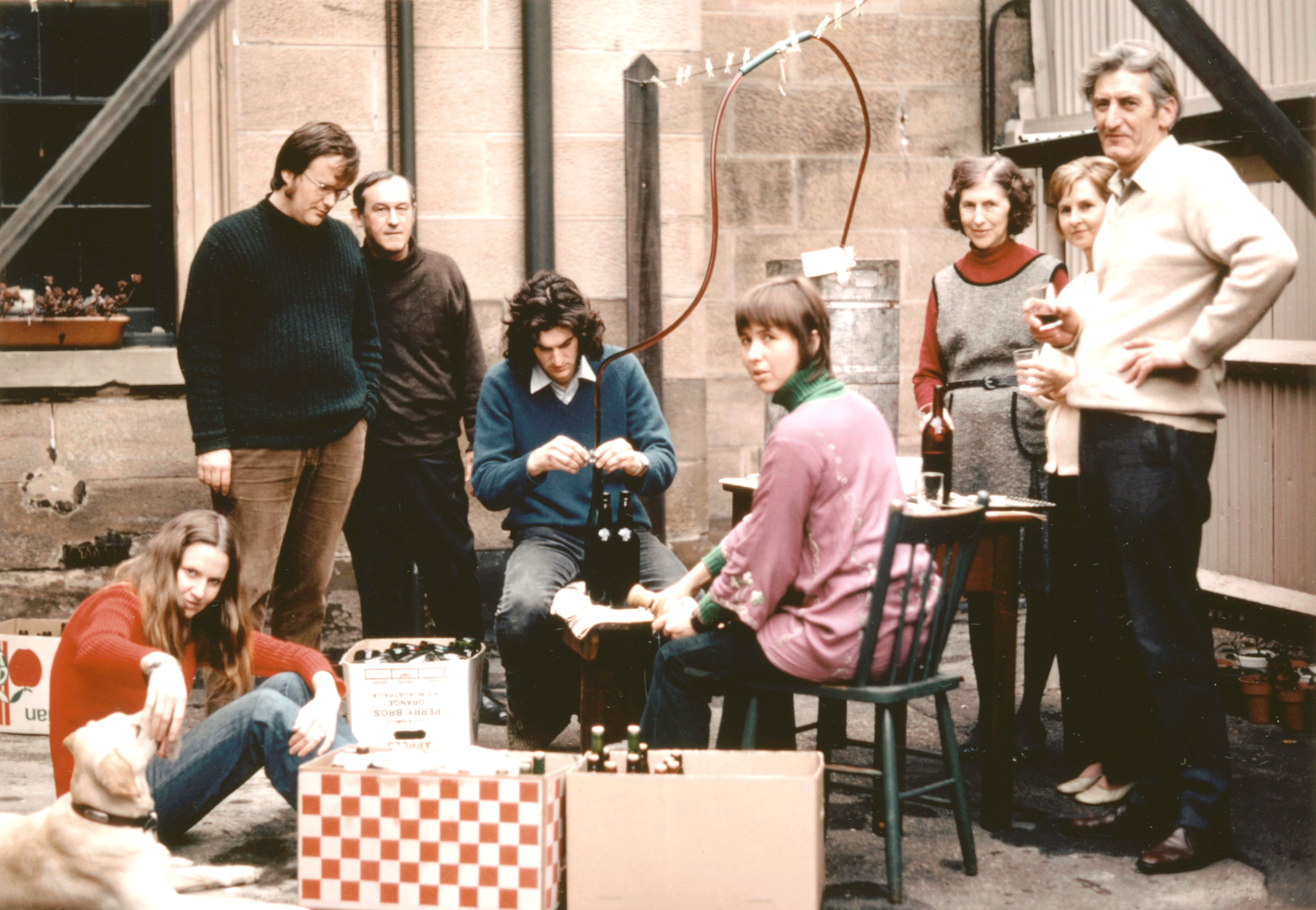 Group of people sit outside in a courtyard bottling wine.