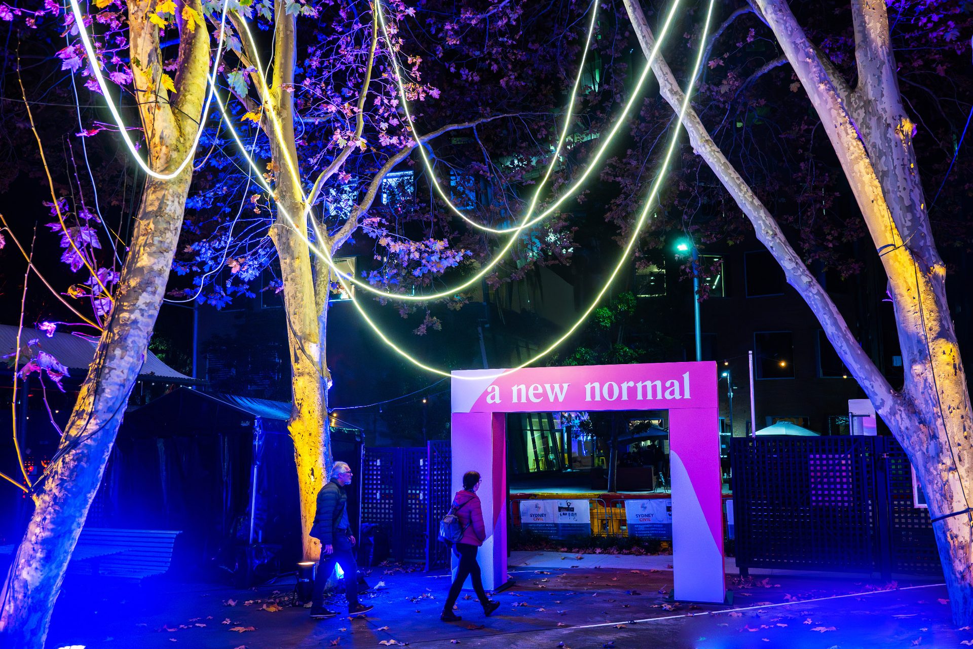'A New Normal' entrance banner amongst colourfully lit trees in a courtyard.