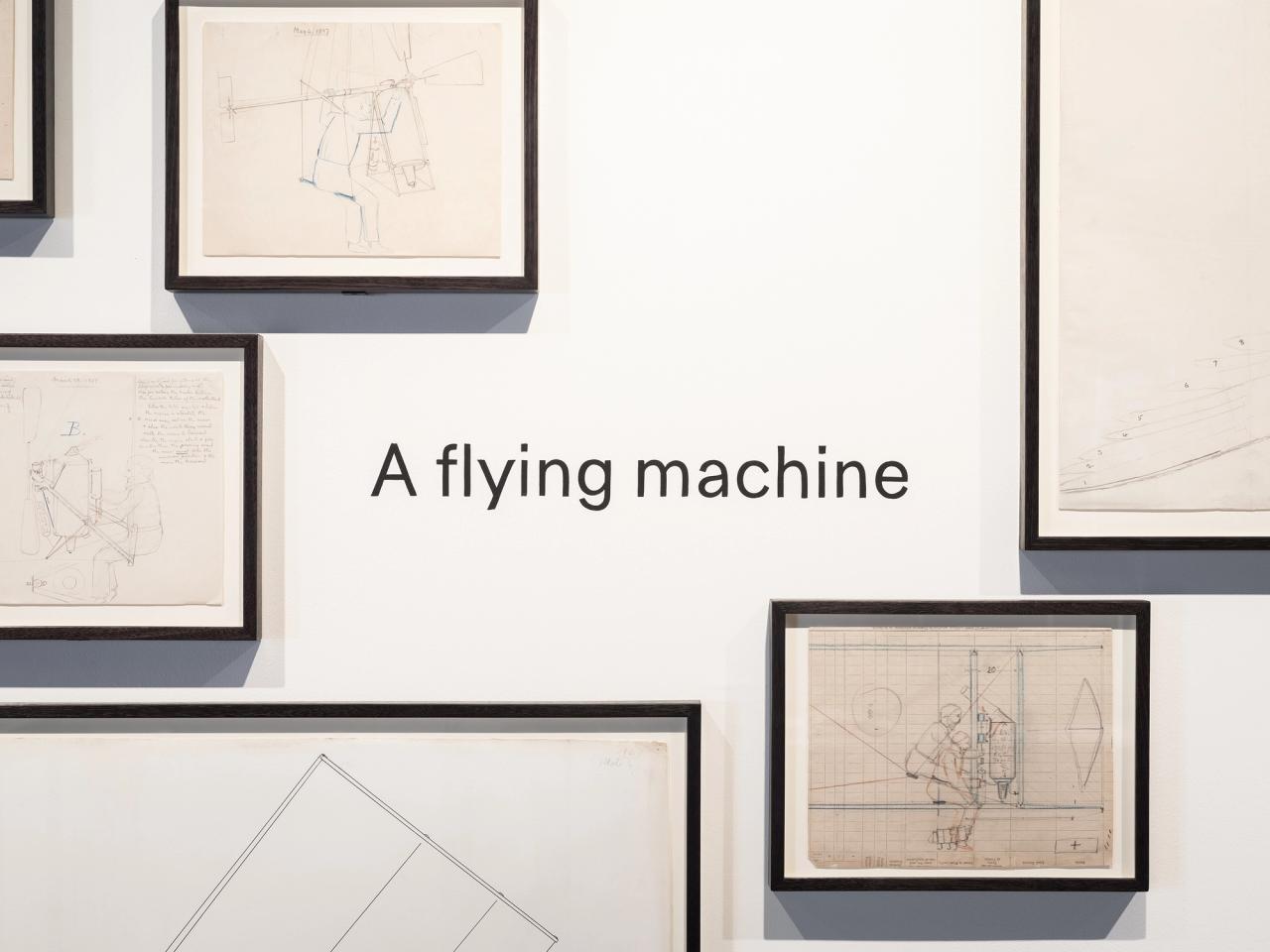 A wall of framed drawings surround the phrase A flying machine