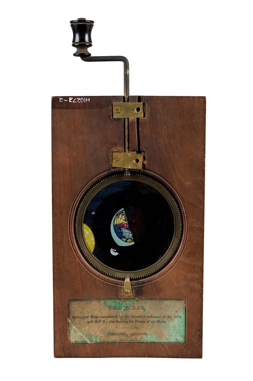 Small wooden device with a turn handle, with a gear system that would rotate a central circular panel. Inside the panel is a simple illustration of the Sun, Moon and Earth.