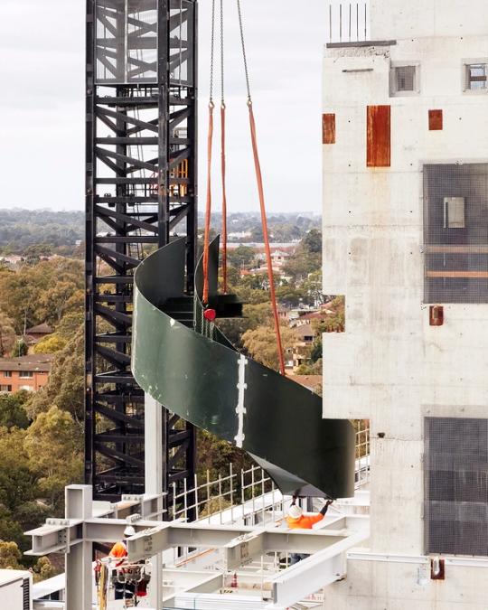 Staircase getting lifted down by crane into construction site.