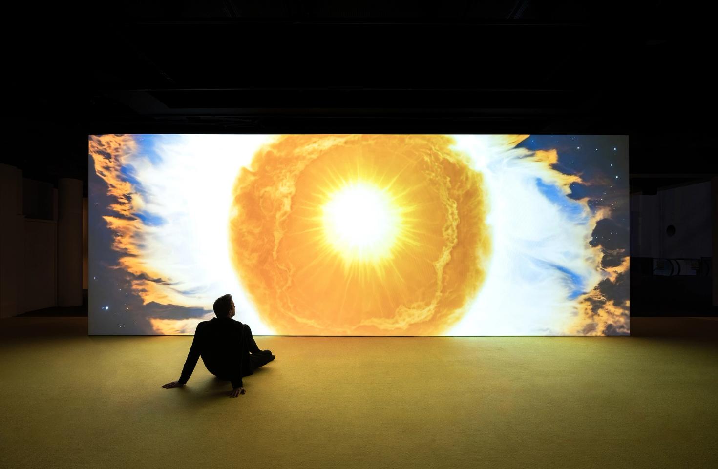 Man sits in front of projection of sun drawing