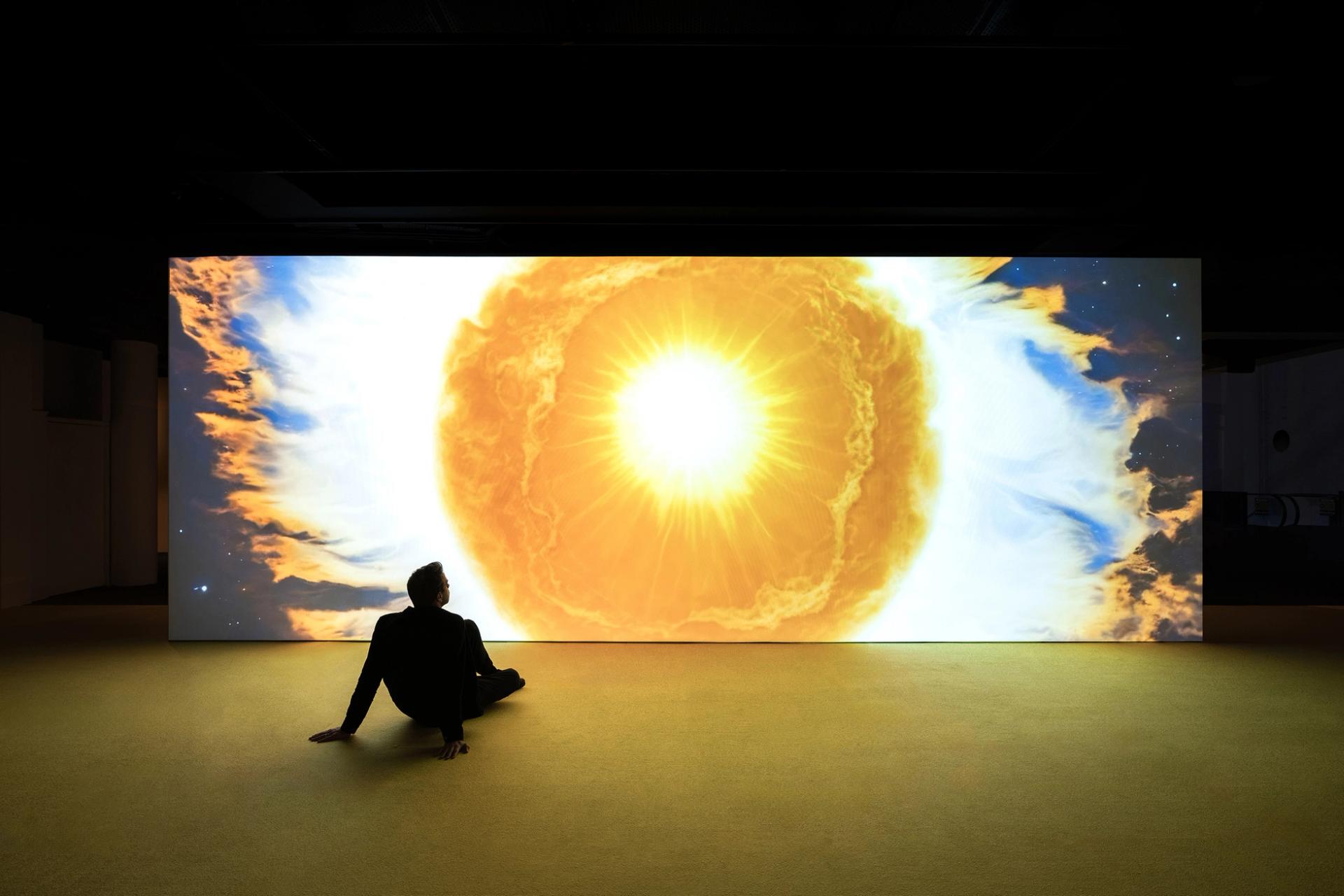 Man sits in front of projection of sun drawing