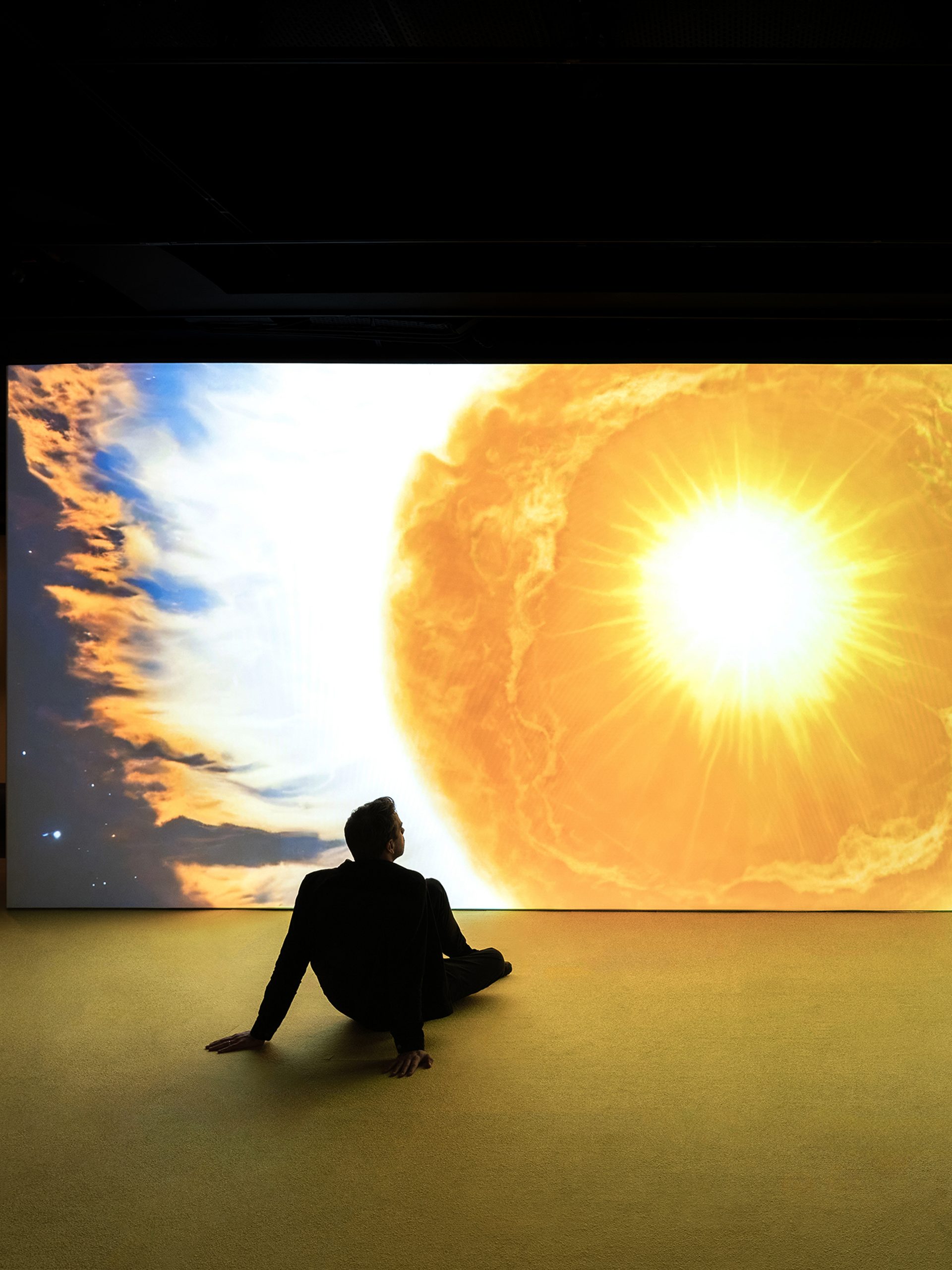 Man sits in front of projection of sun drawing