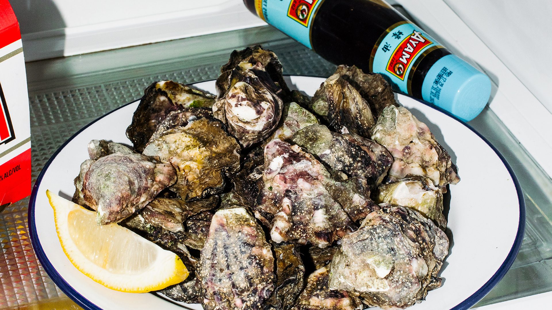 A plate of unchecked oysters with a slice of lemon on a white plate in a fridge.