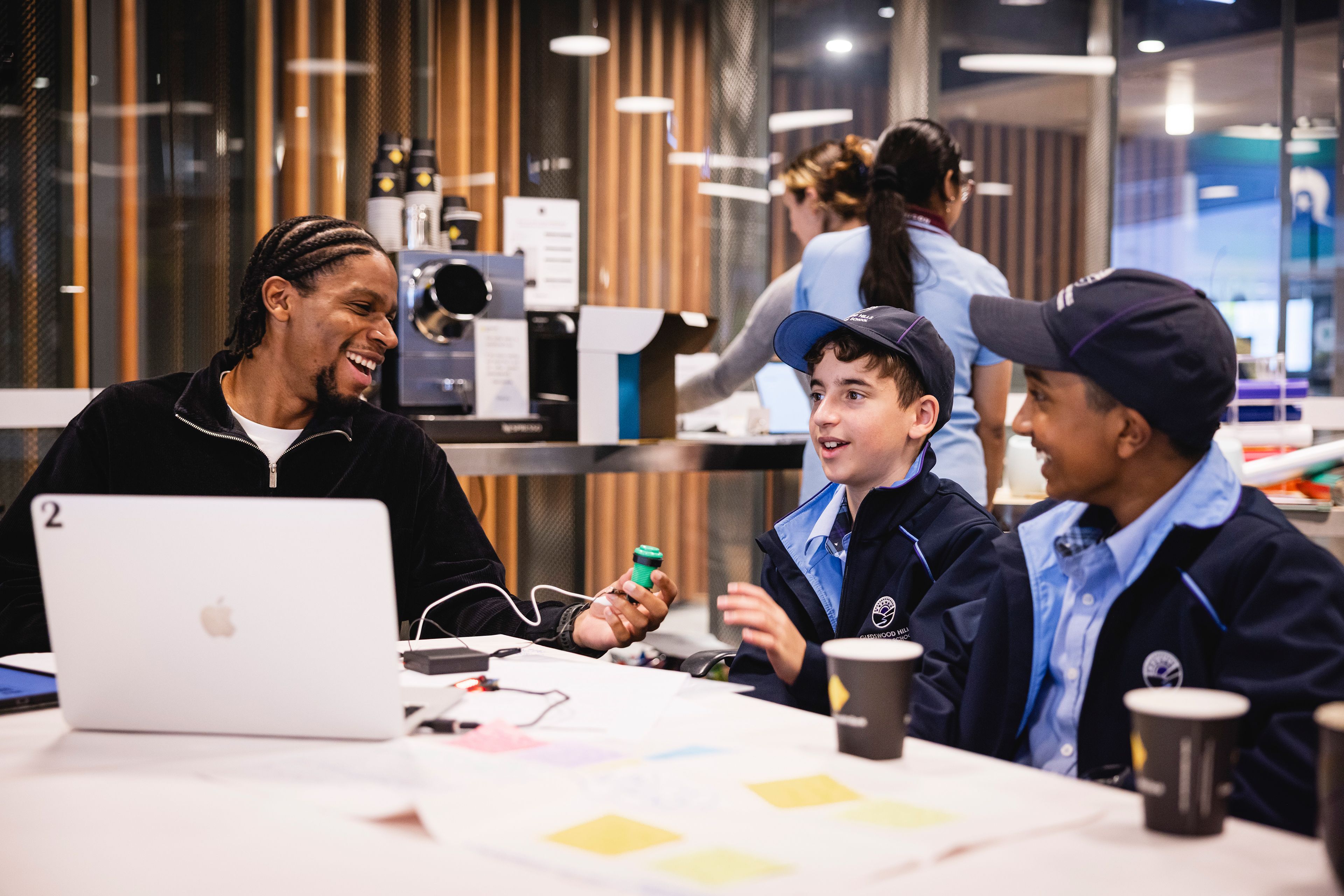 Photo of 2 students and a teacher working together, with mechanical parts and a laptop in front of them