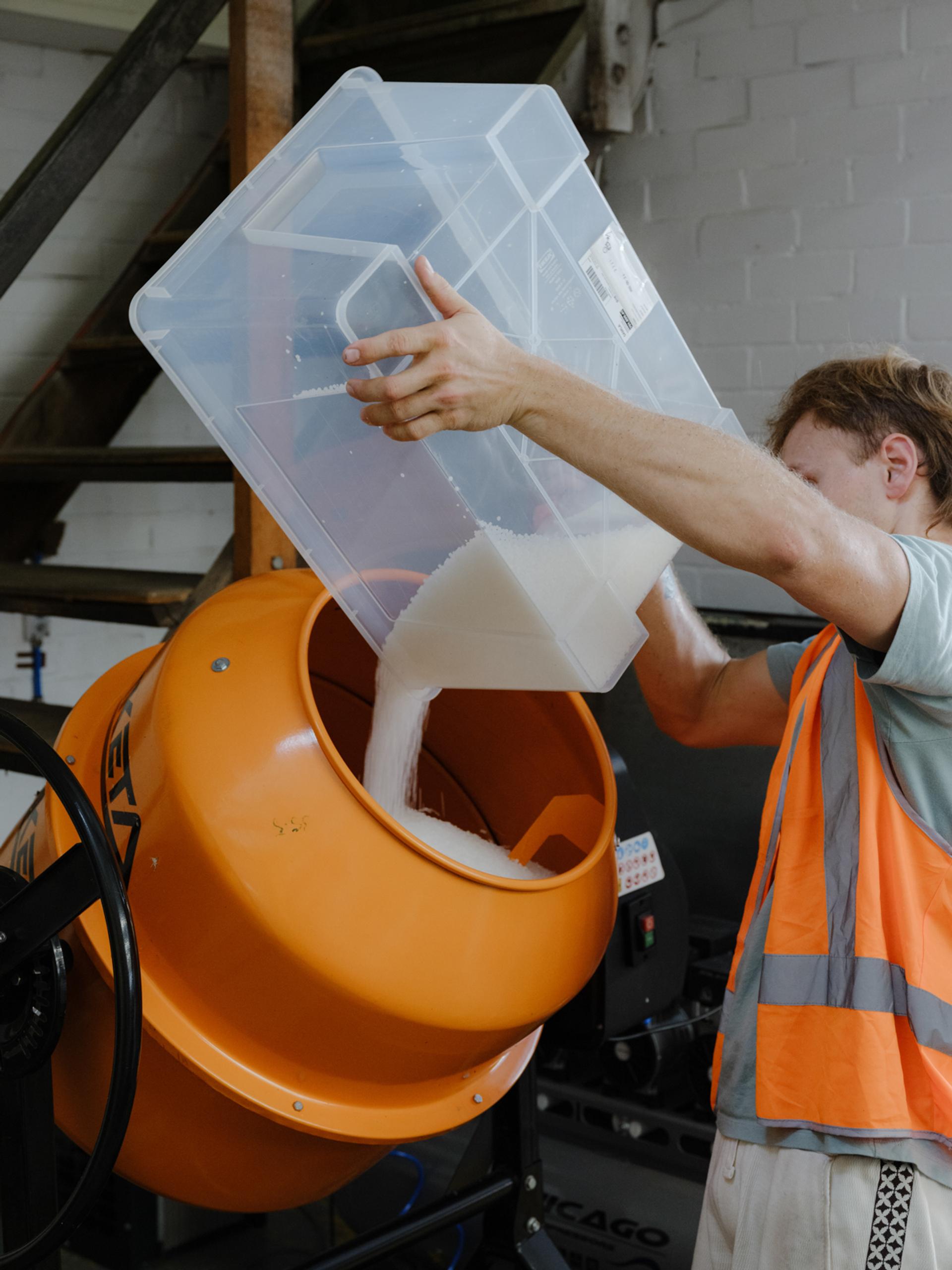 Figure pours plastic bits into a rotating mixer.